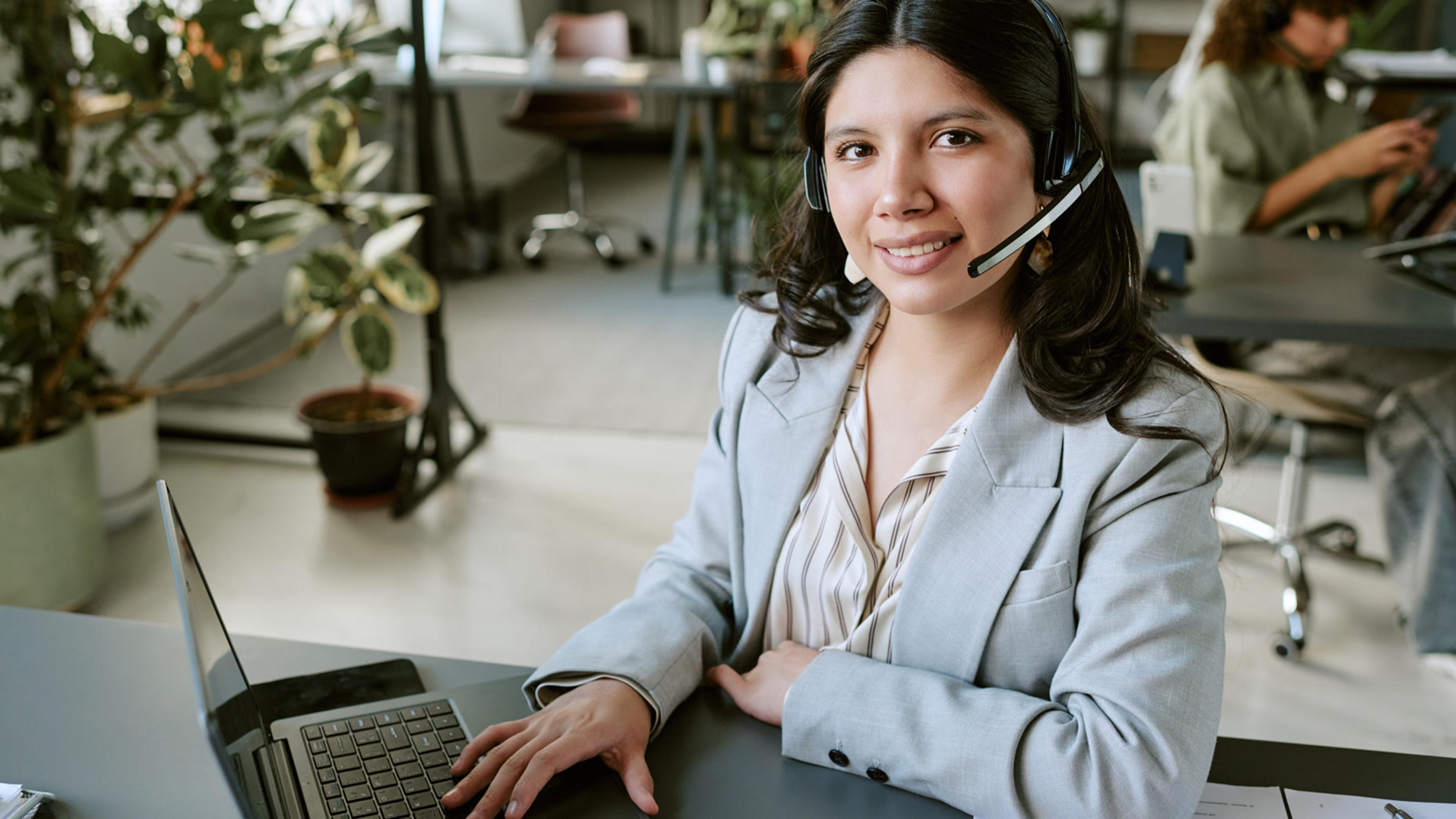 Professional young woman with a headset smiling at her office desk on a softphone