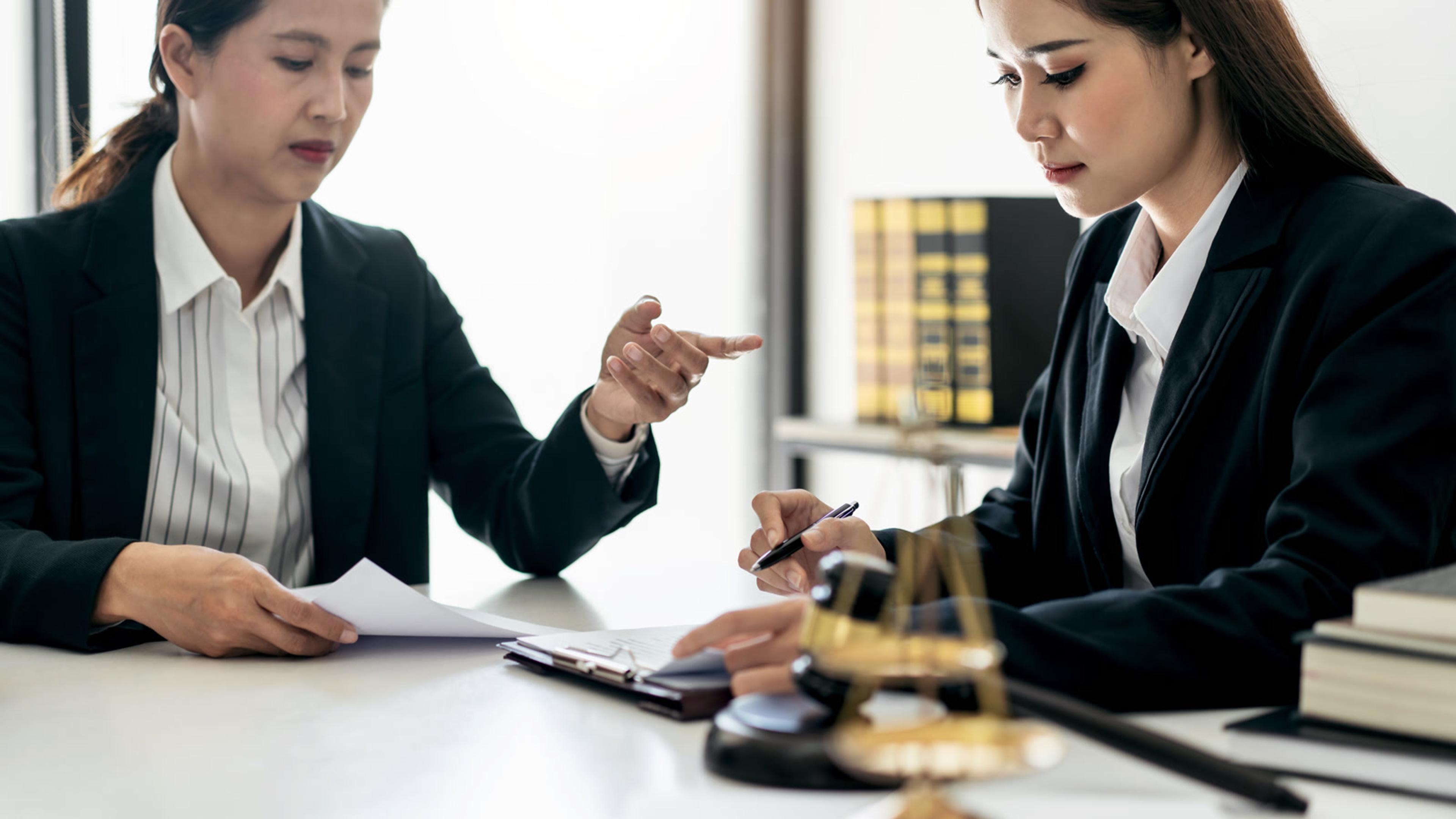 Two businesswomen reviewing and signing documents at a desk — acceptable use policy acknowledgment