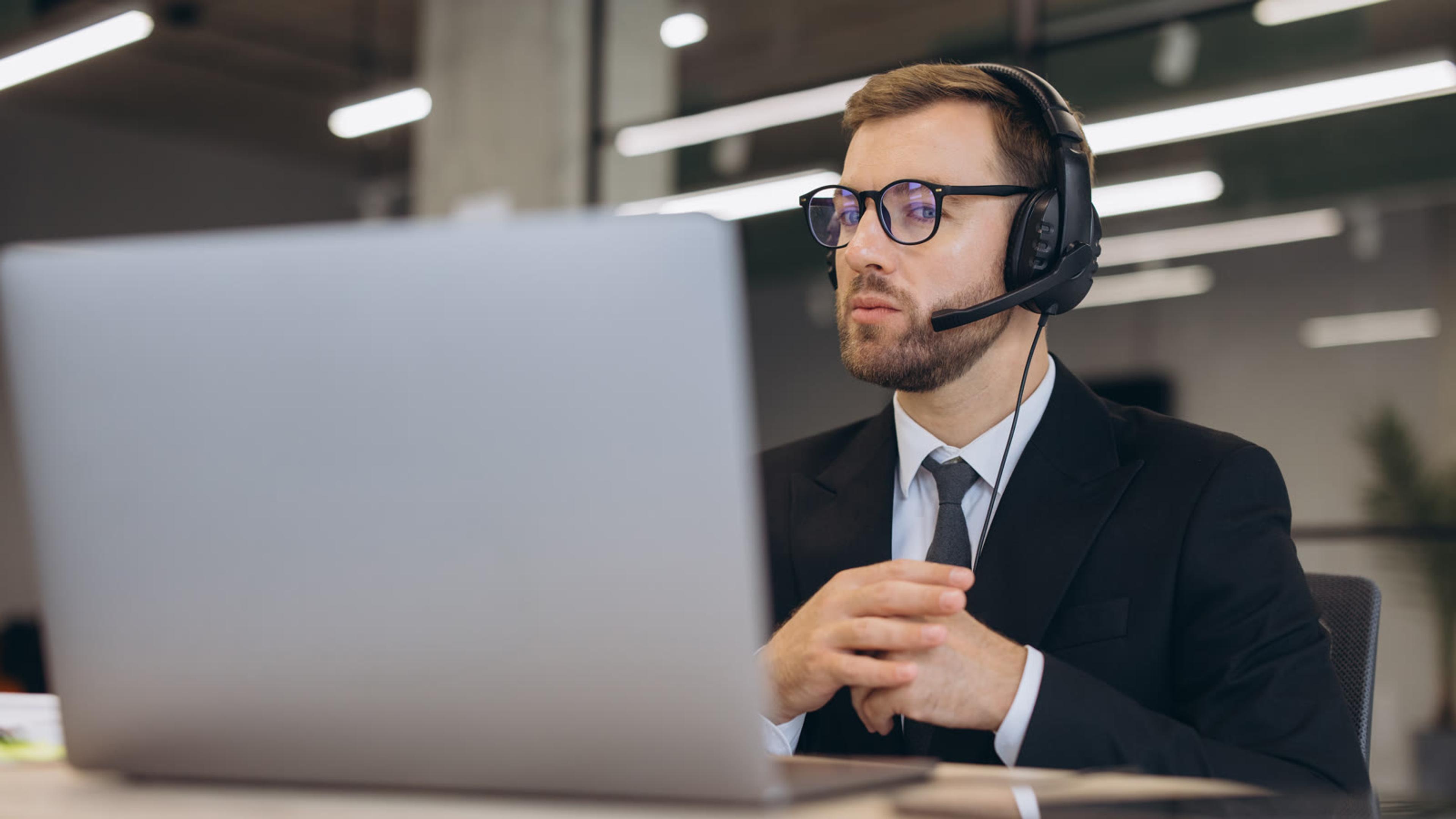 Businessman on a headset testing calls on a laptop in an office