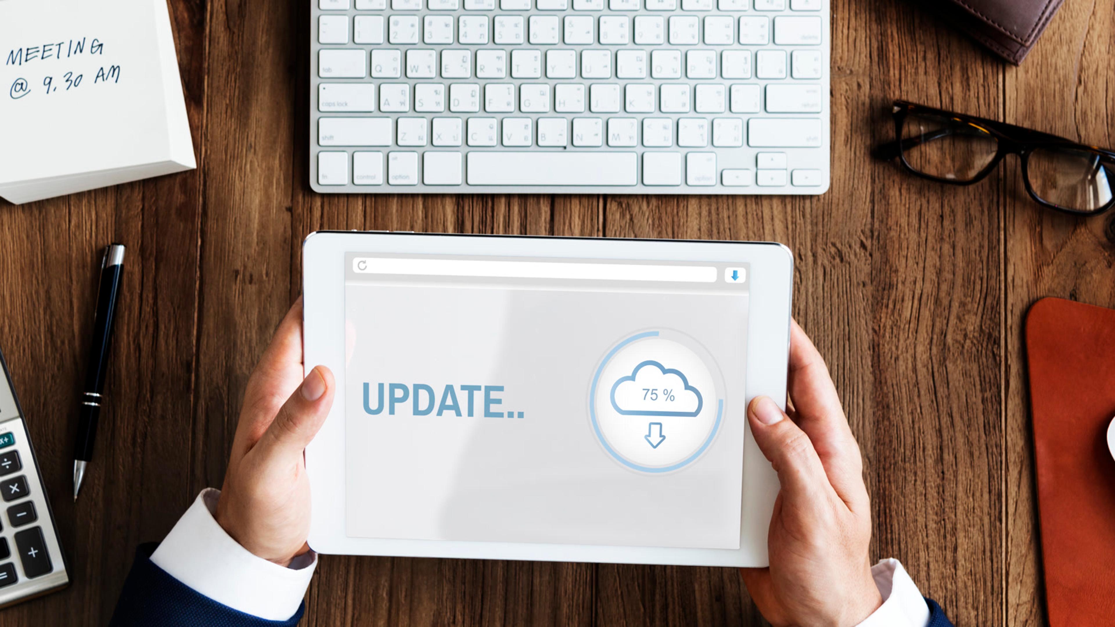 Office worker holding a tablet displaying a software update progress screen — endpoint patch cadence