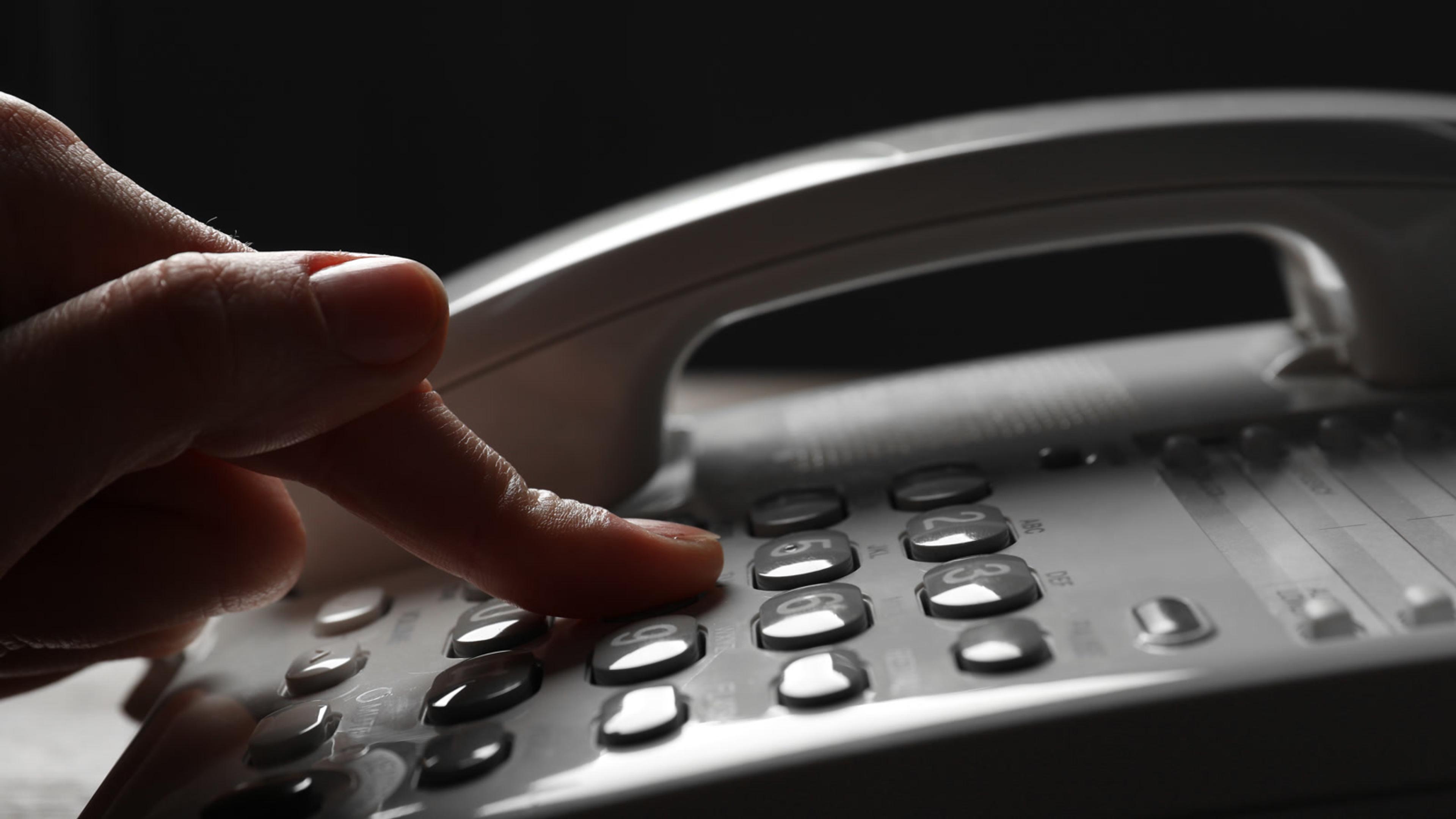 Finger pressing a button on a modern white phone for IVR menu input