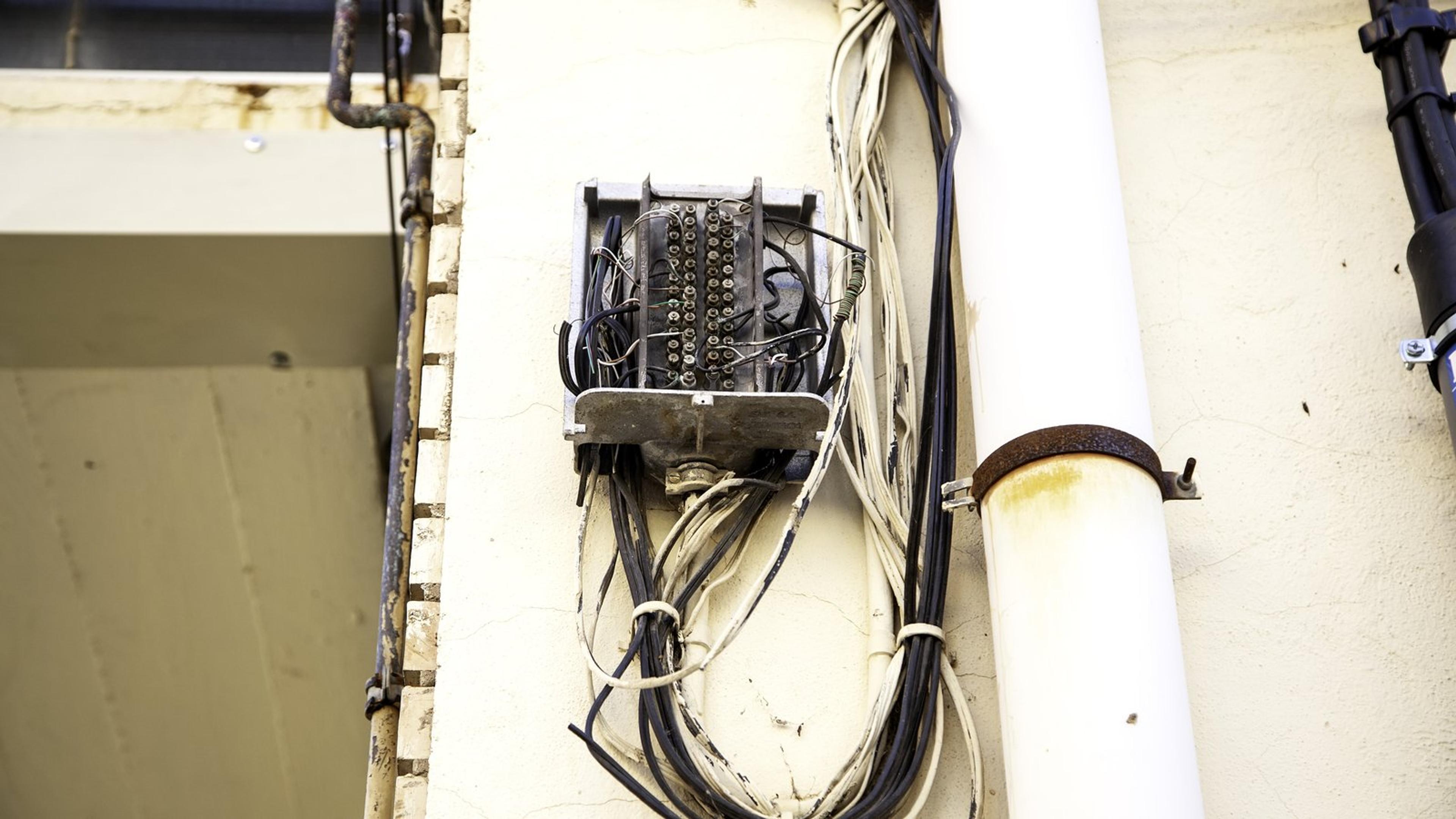 Open wall-mounted junction box with bundles of old copper cables running down a building wall