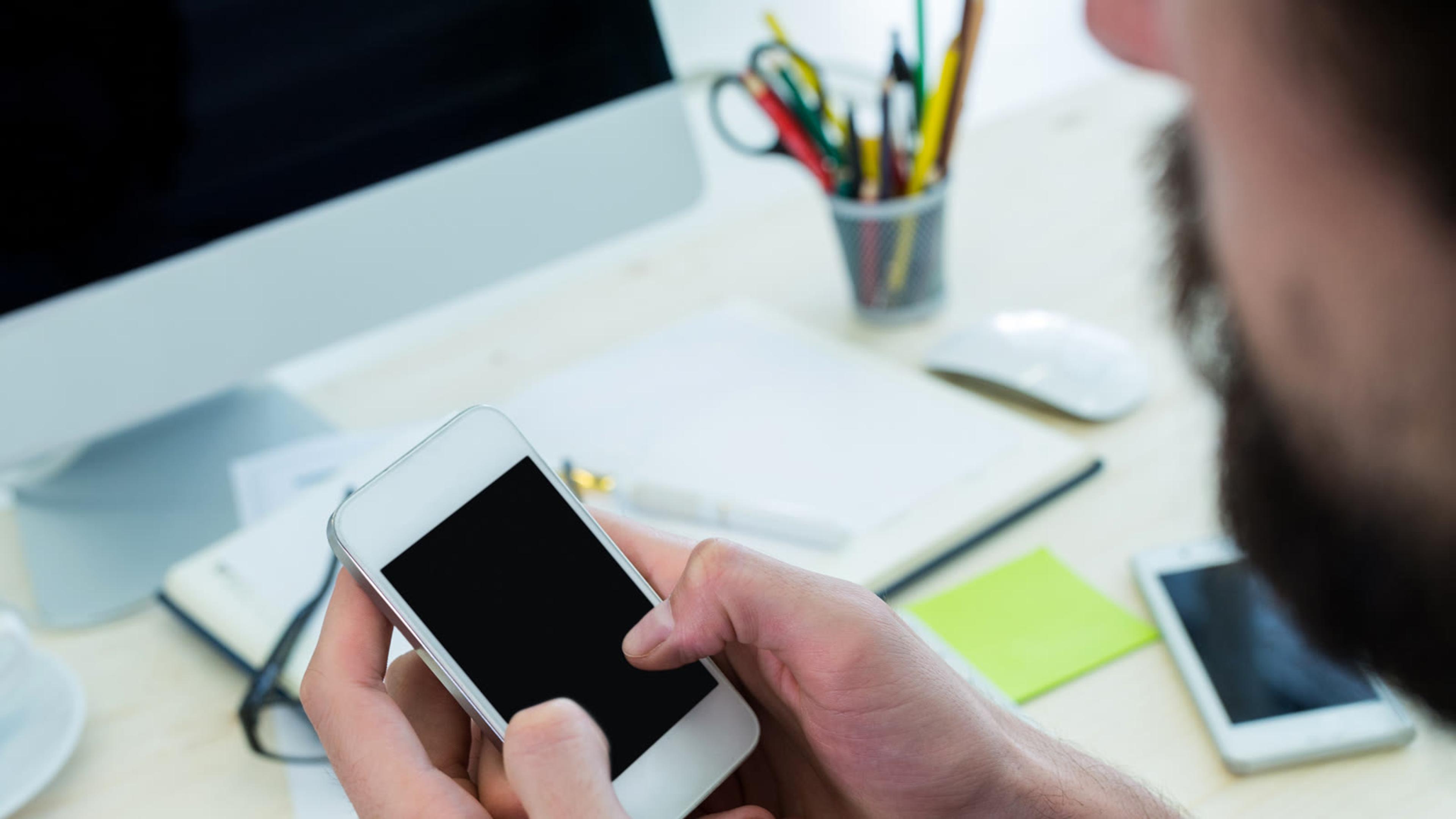 Man using a smartphone at a wooden desk in an office for authenticator-based MFA