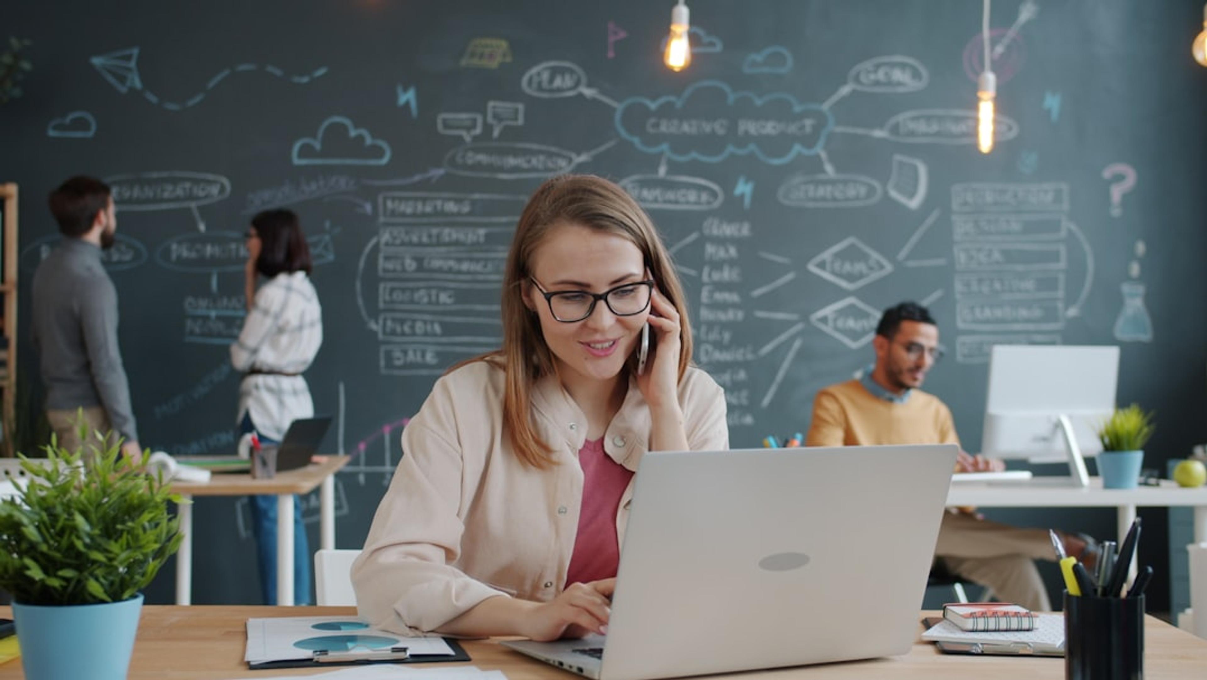 Business user taking calls on a smartphone beside a laptop in a modern office