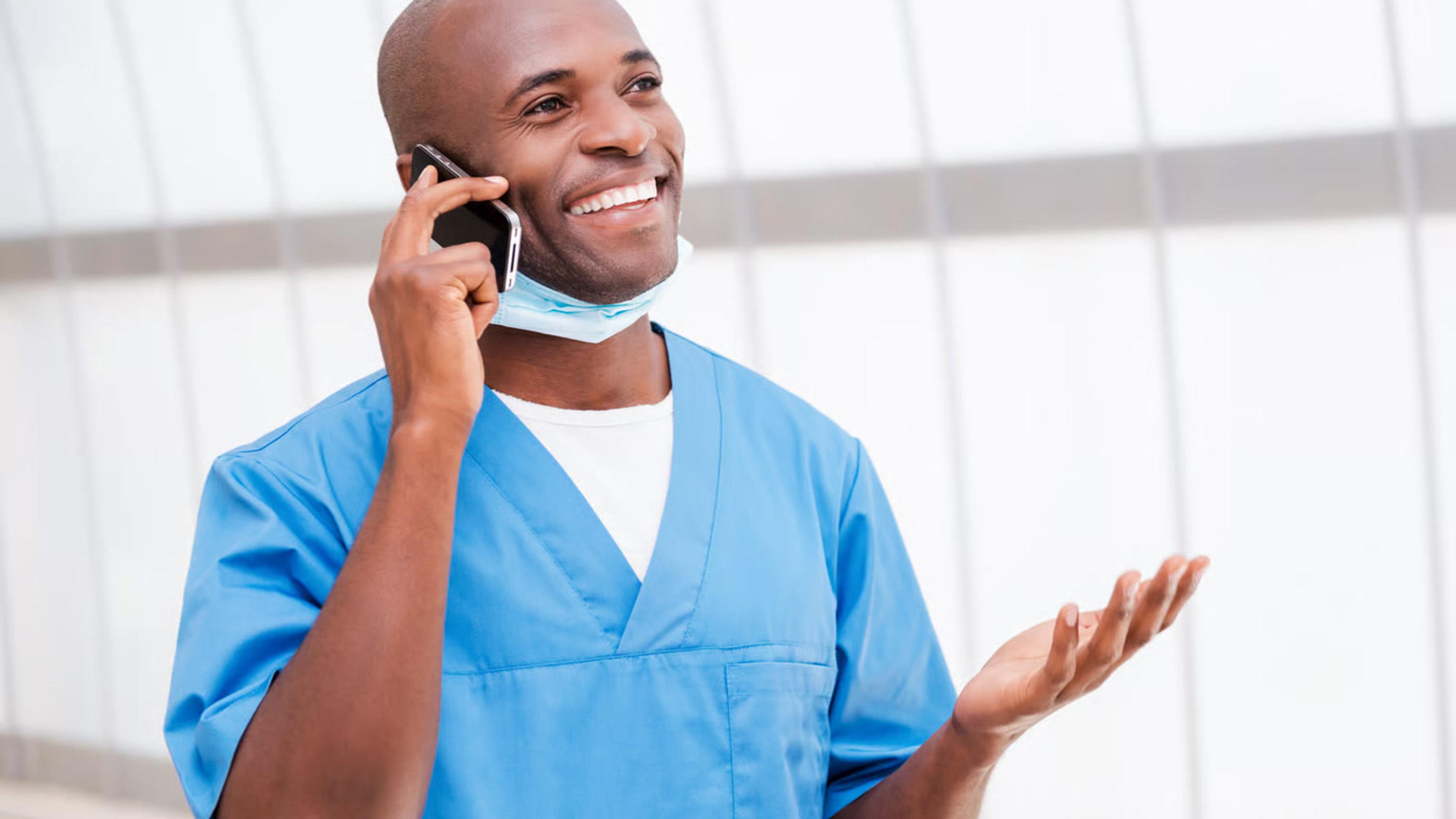 Smiling clinician in scrubs talking on a cell phone for secure healthcare VoIP