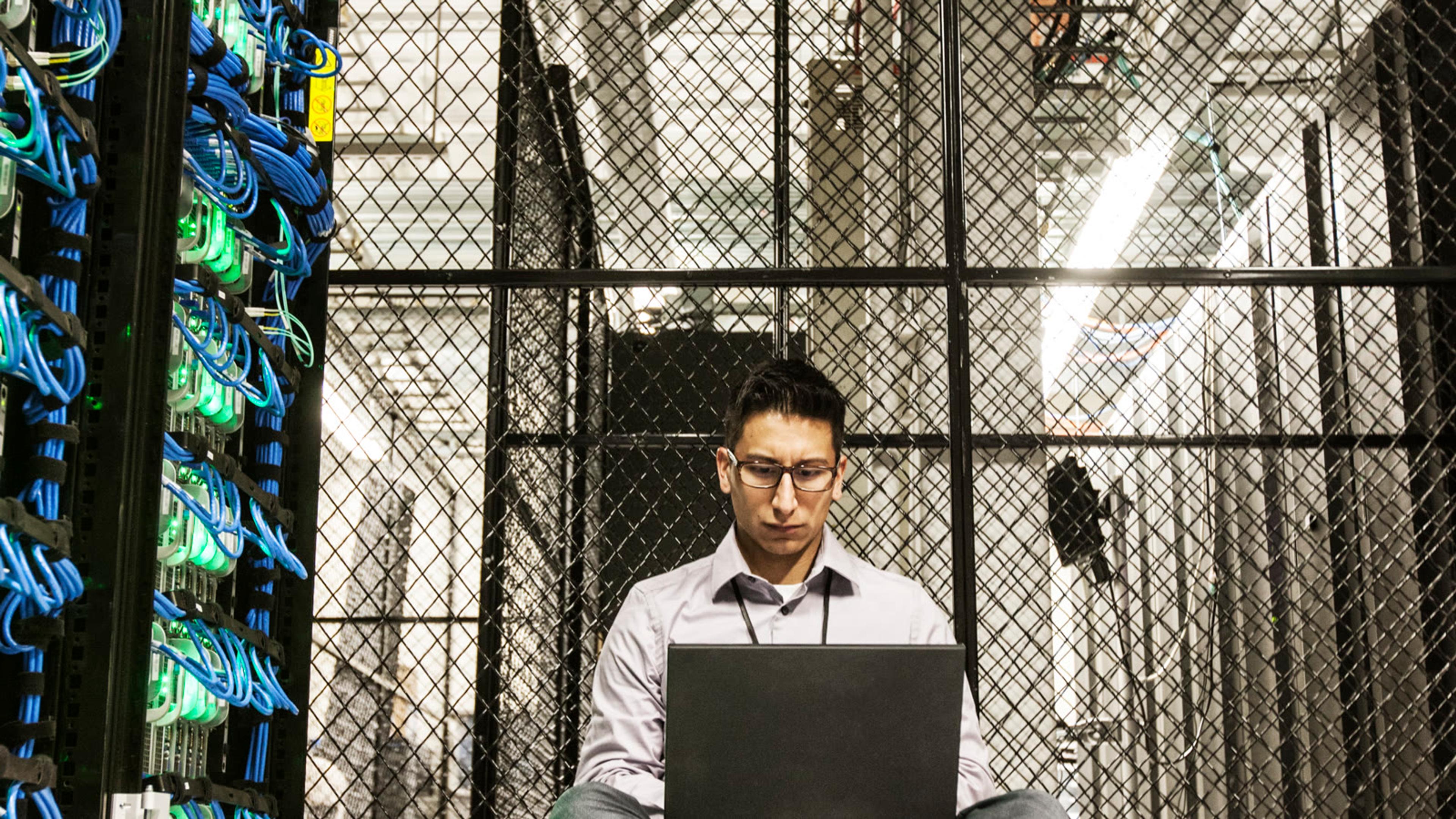 IT technician working on a laptop in a data center — FreePBX PBX admin/server setup for mobile softphones