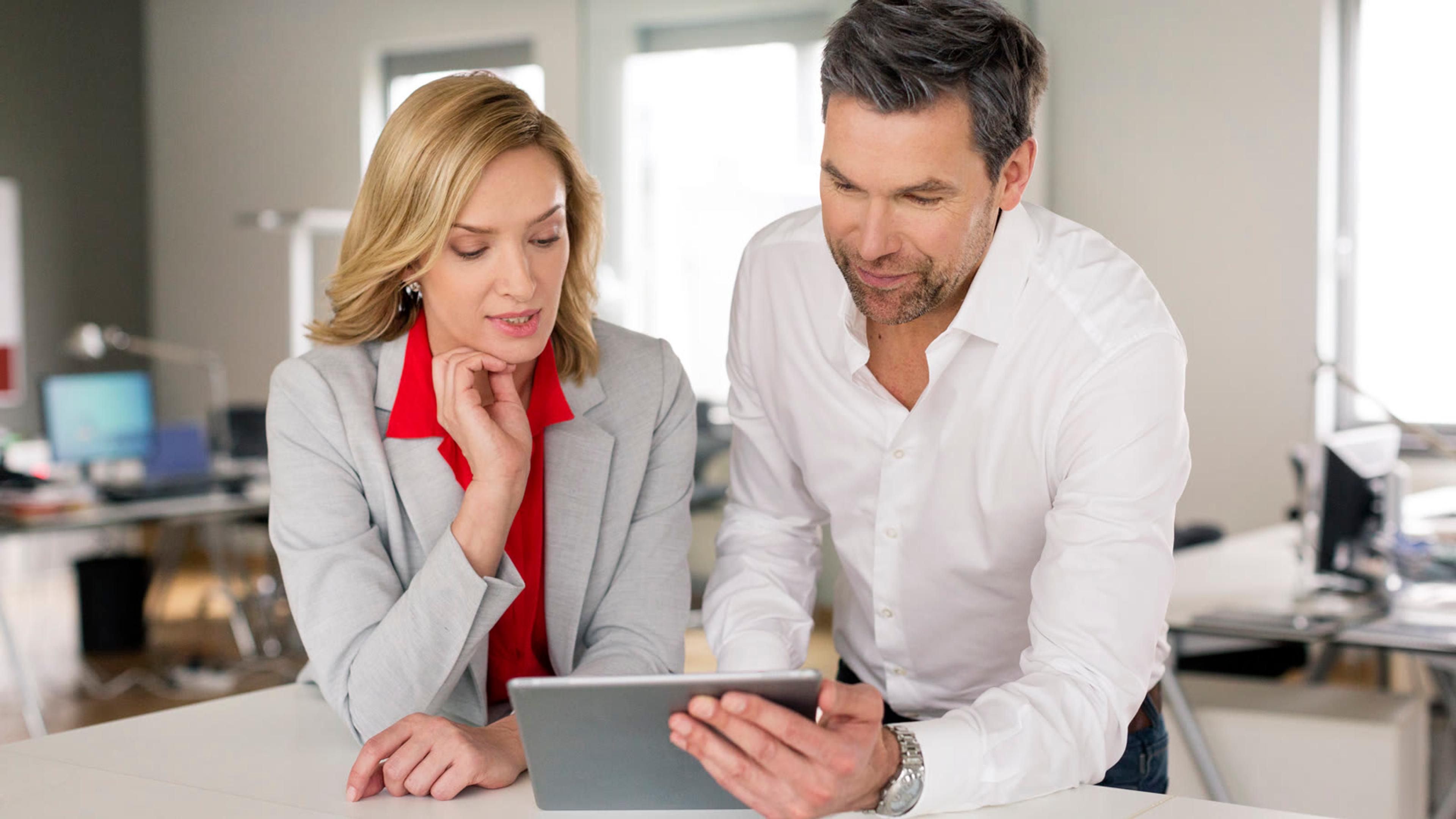 Two colleagues leaning over a desk to review a change together on a tablet