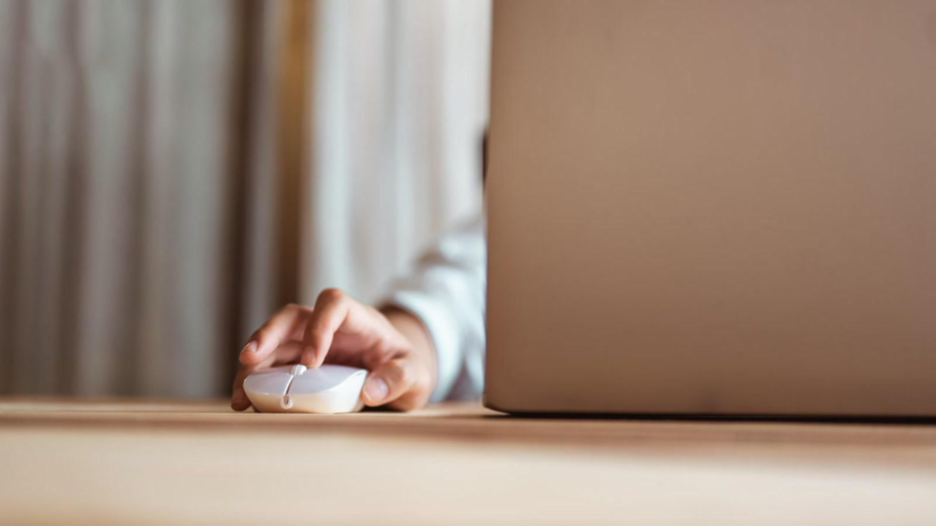 Hand using a mouse next to a laptop — desktop click-to-call for SIP softphones