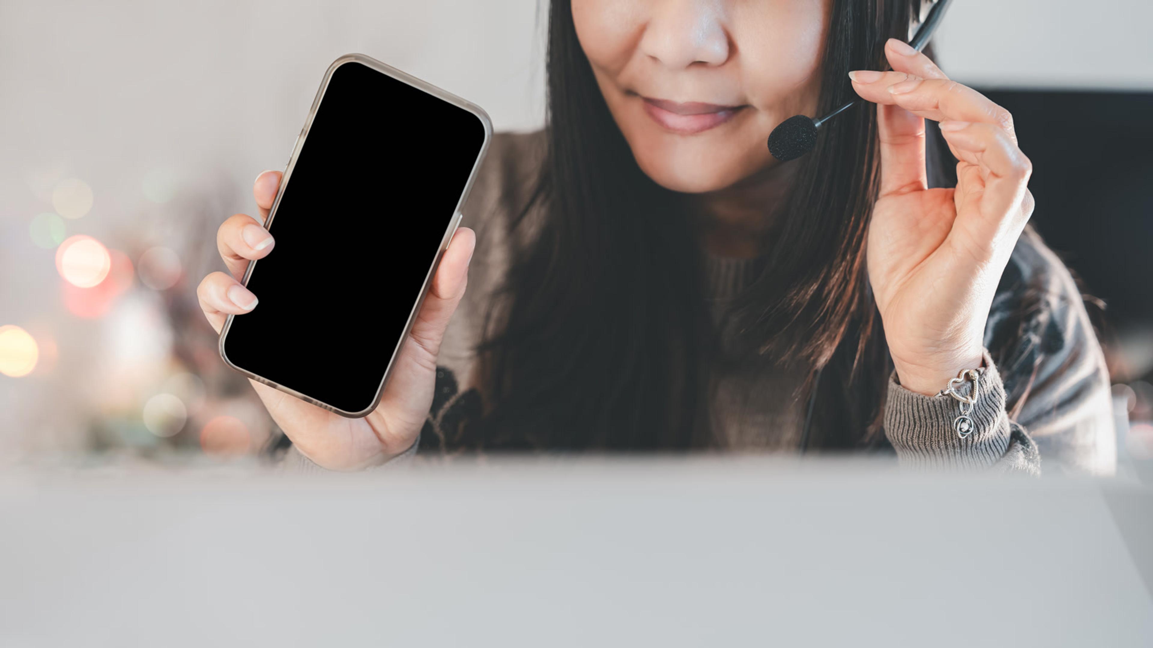 Smiling woman holding a phone while wearing a headset — mobile softphone setup for business