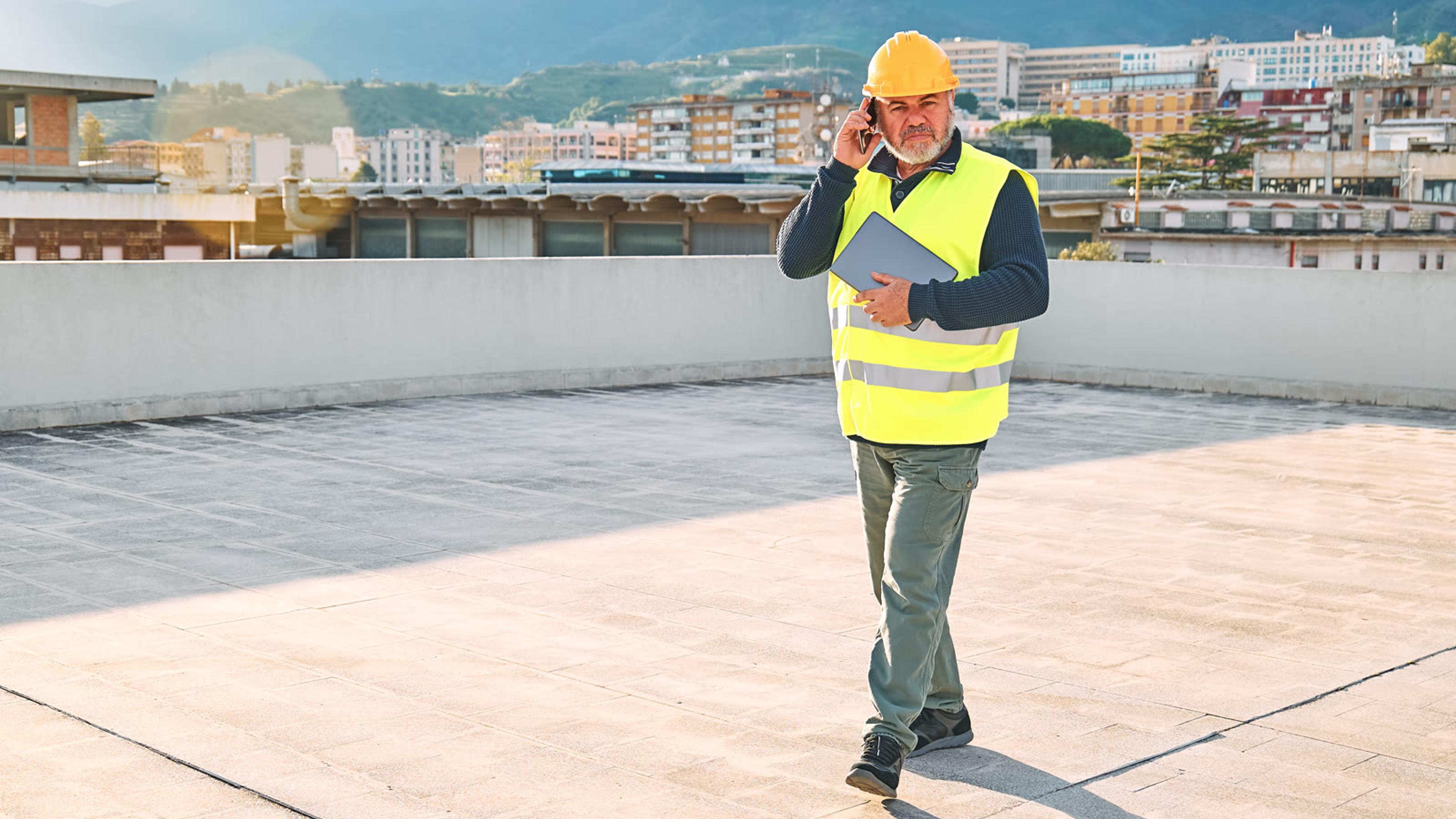 Construction supervisor making a smartphone call on a rooftop — field team mobile VoIP calling