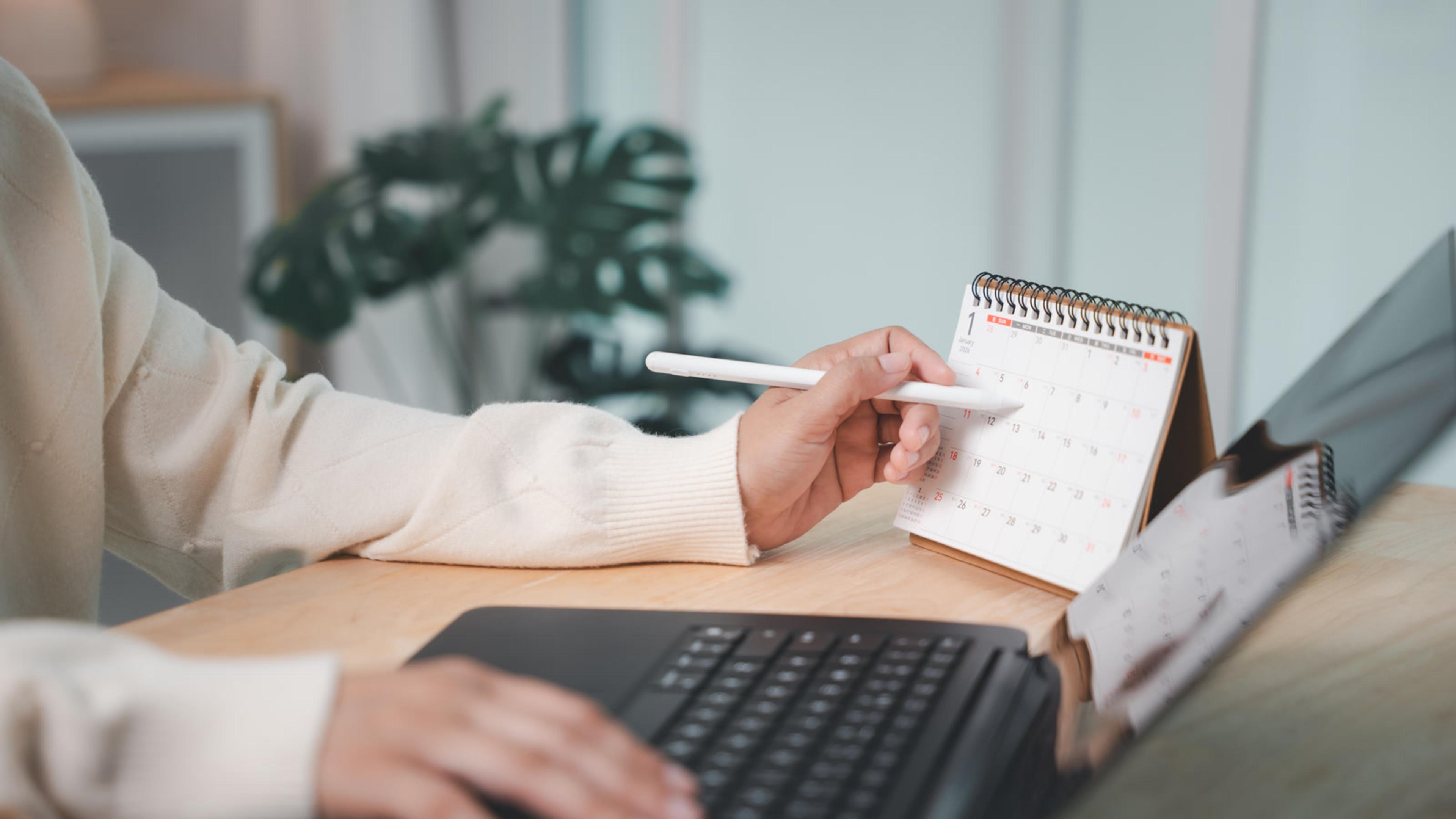 Person pointing to a desk calendar beside an open laptop — software-renewal planning and license-hygiene reviews