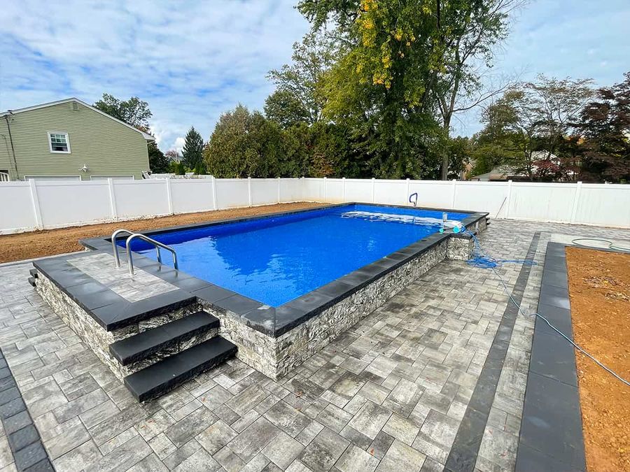 Raised above ground pool with gray stone veneer and modern deck
