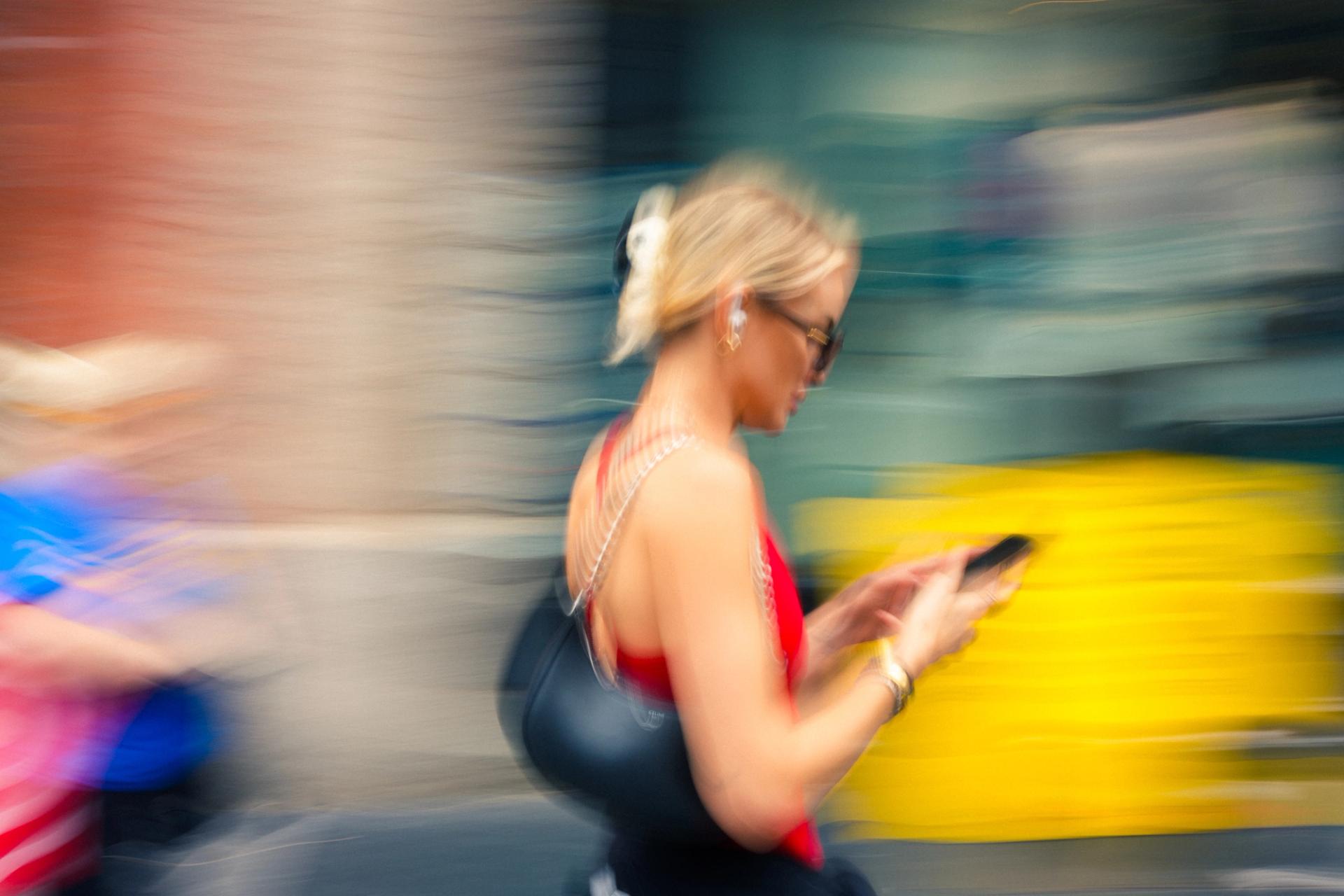 Woman walking while looking at her phone, panned sharp against a yellow blur