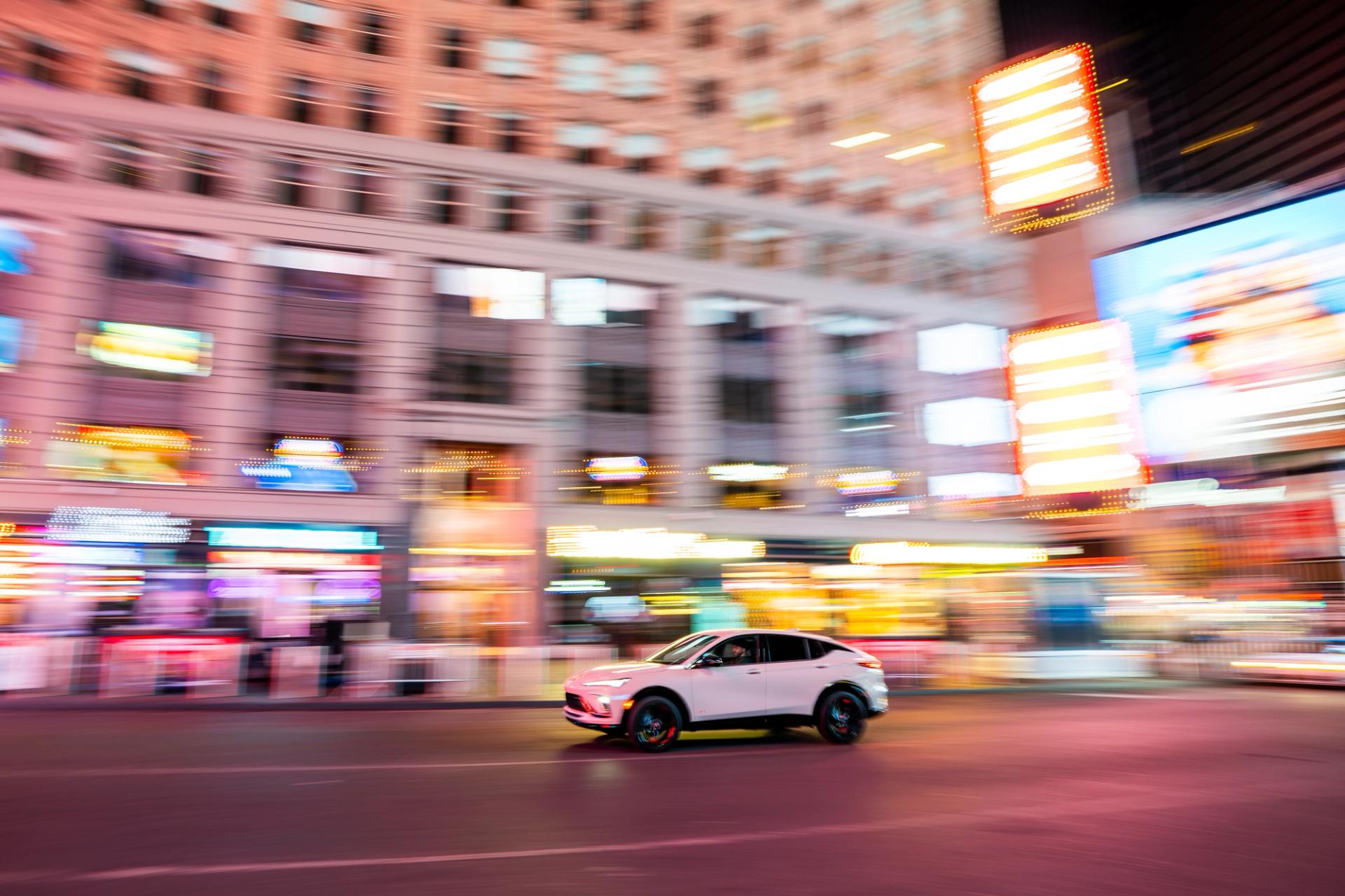 White car panned through Times Square at night, signs smeared into color