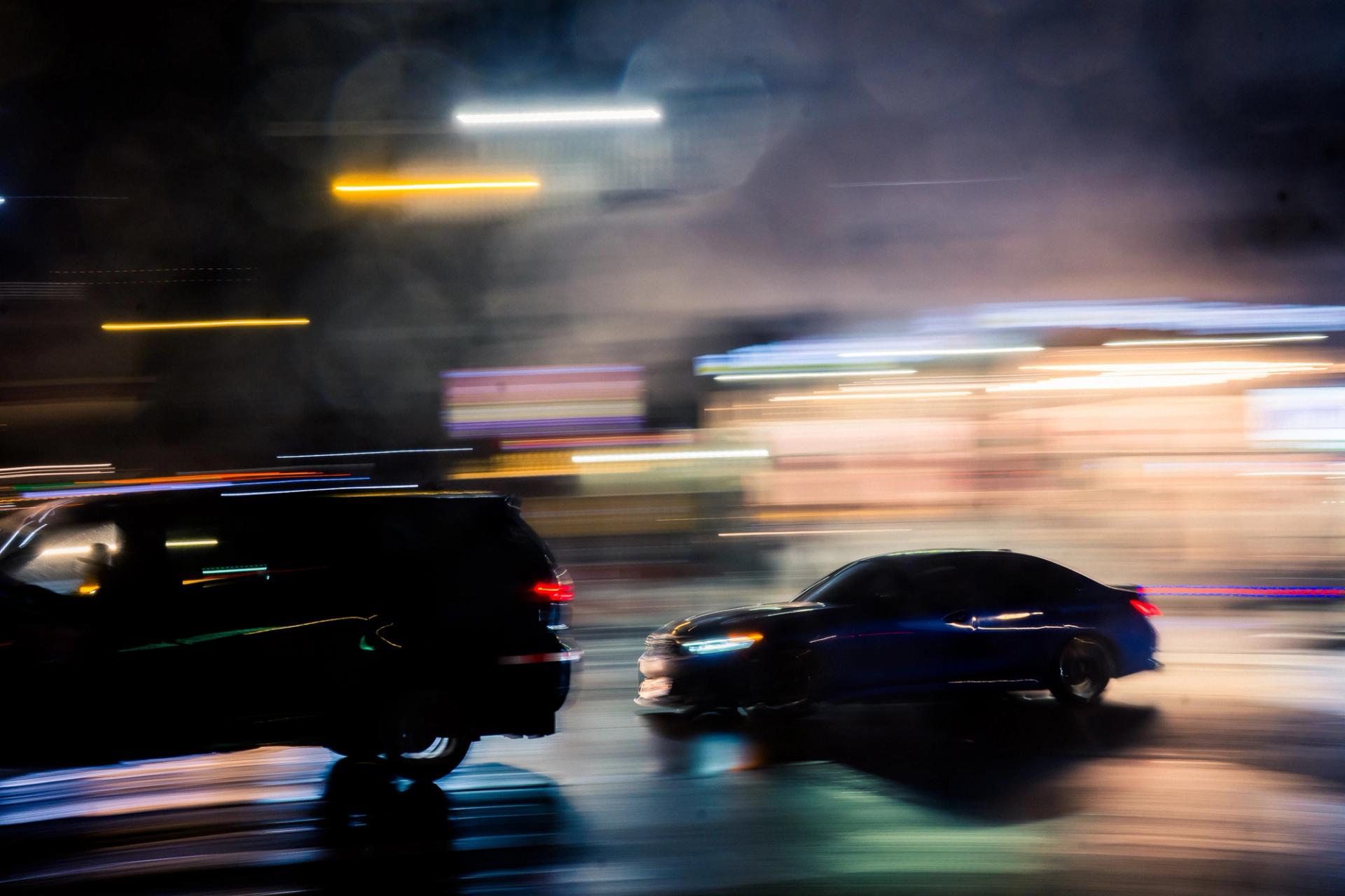Two cars panned at night on a wet street, headlights and streetlights drawn into long streaks
