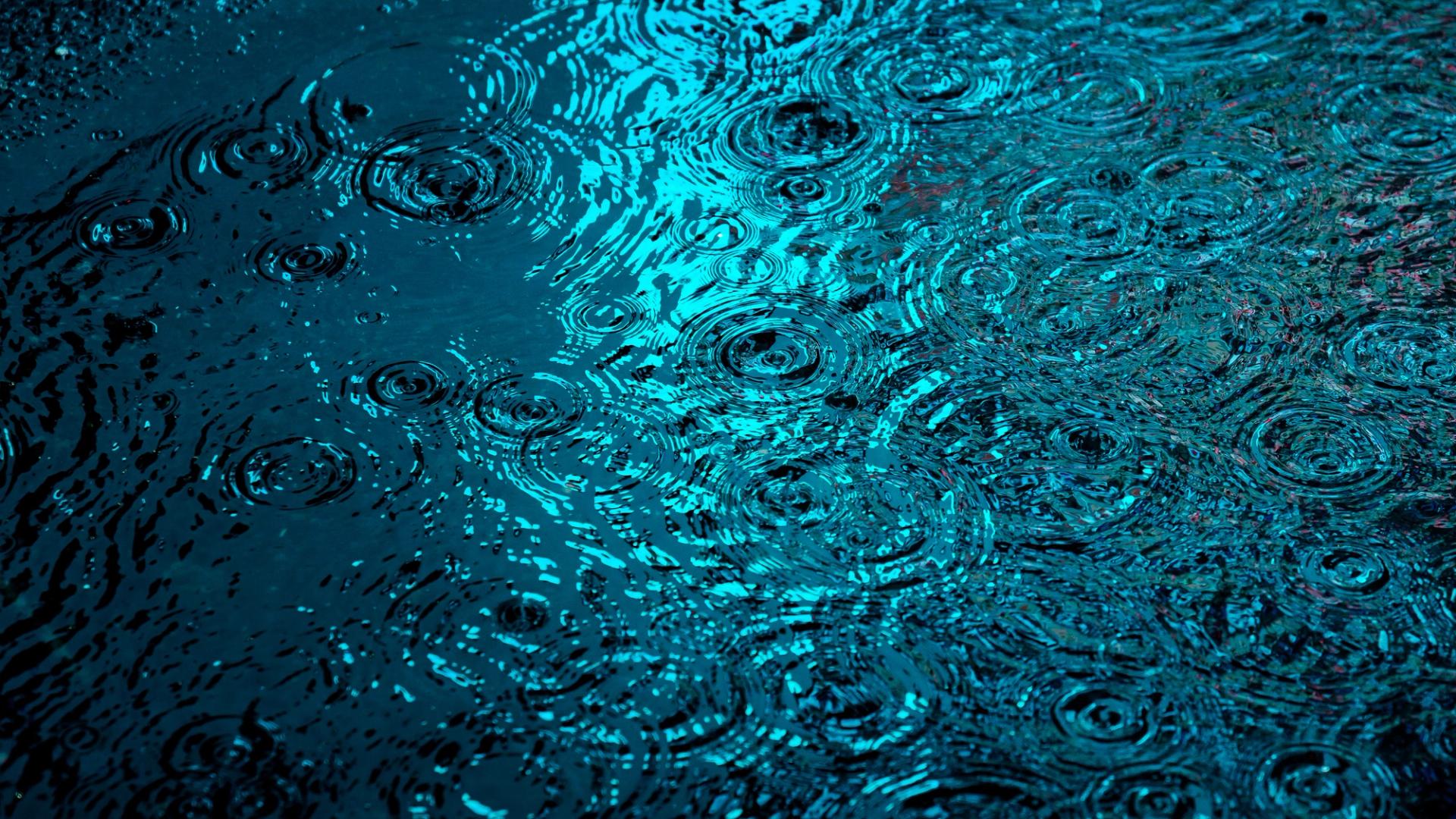 Raindrops frozen mid-splash on a wet street, ripples lit cyan by a passing light