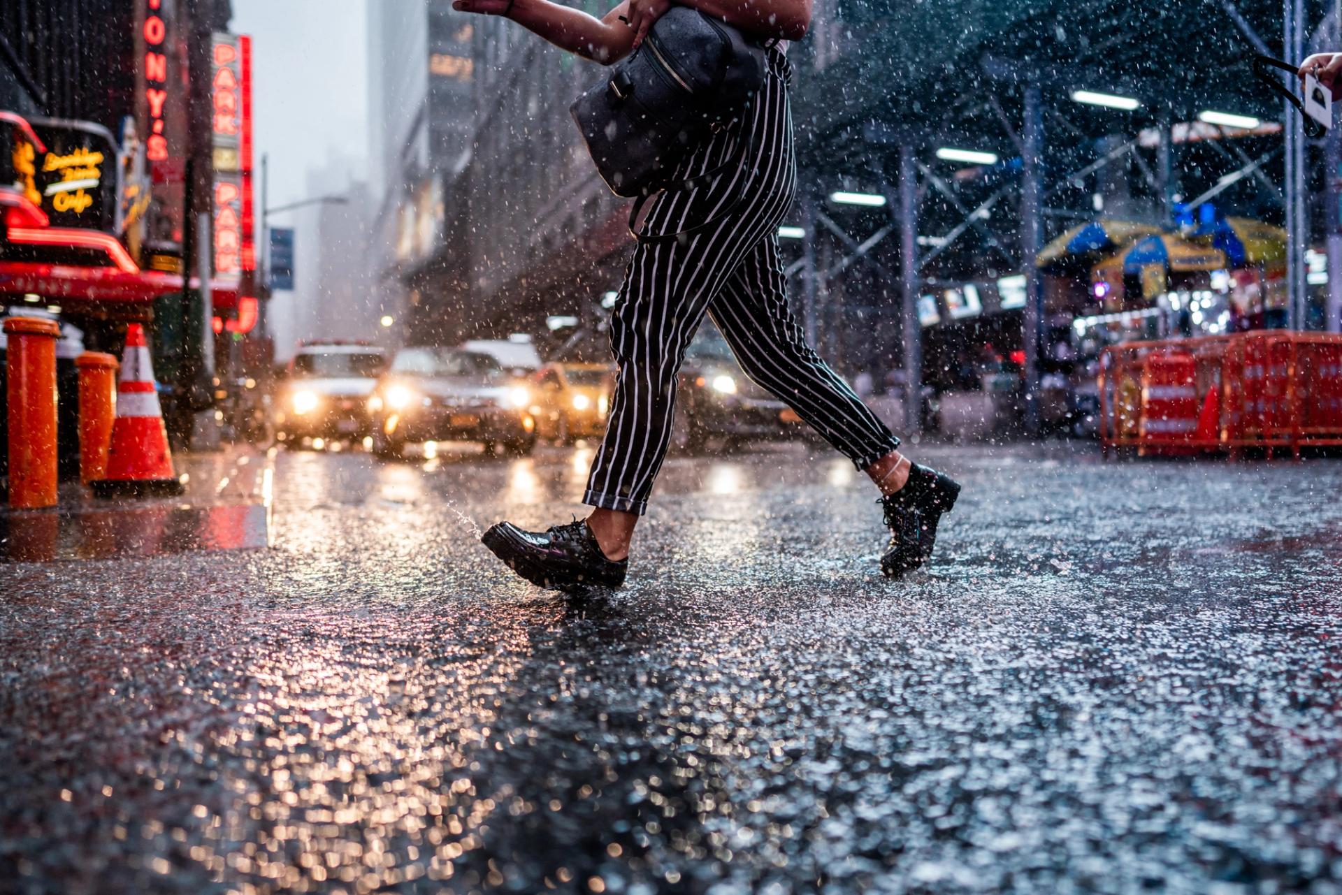 Person in striped trousers striding across a rain-soaked street, every drop frozen mid-air in front of traffic and neon