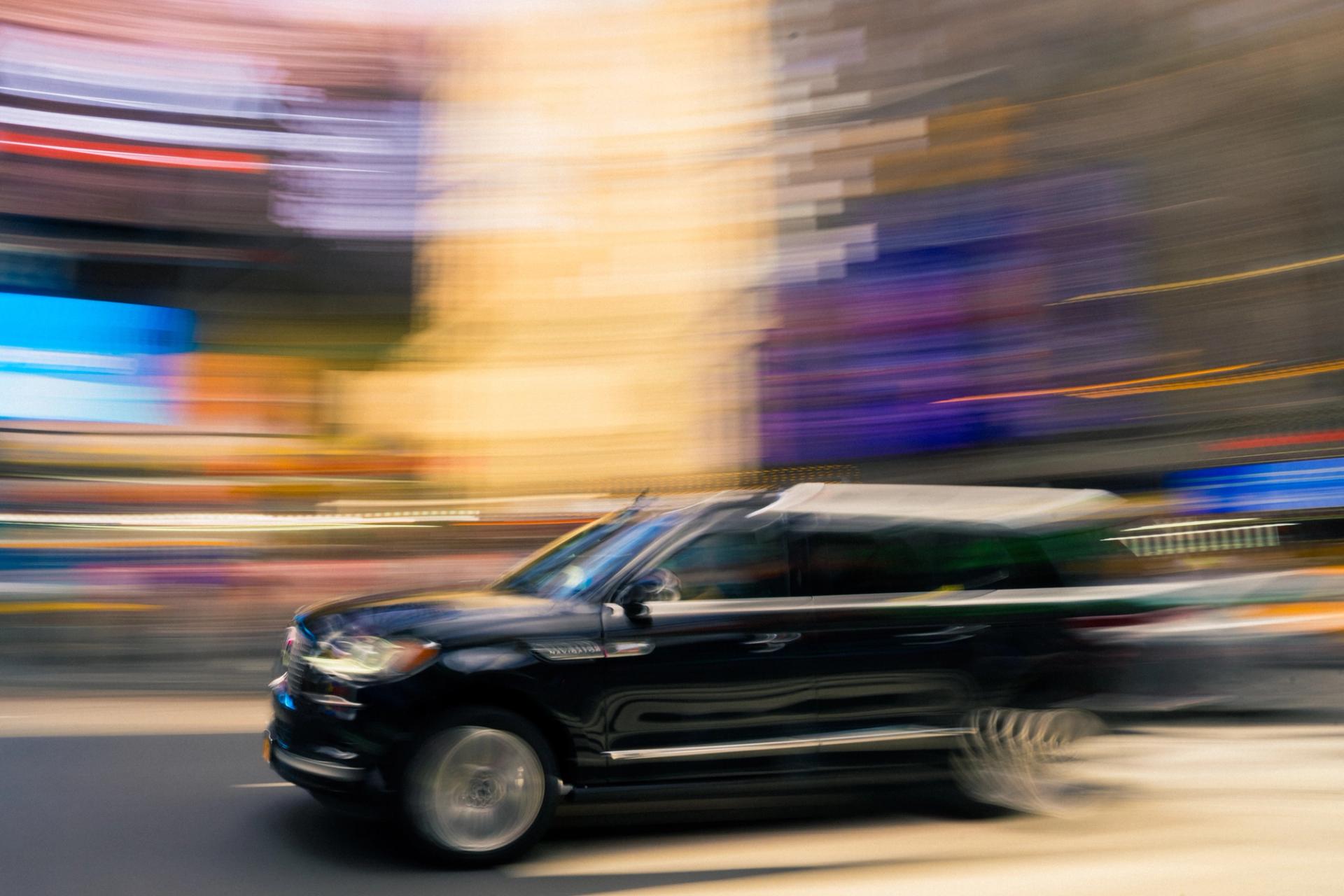 Black SUV panned at slow shutter, background dissolving into streaks of warm light