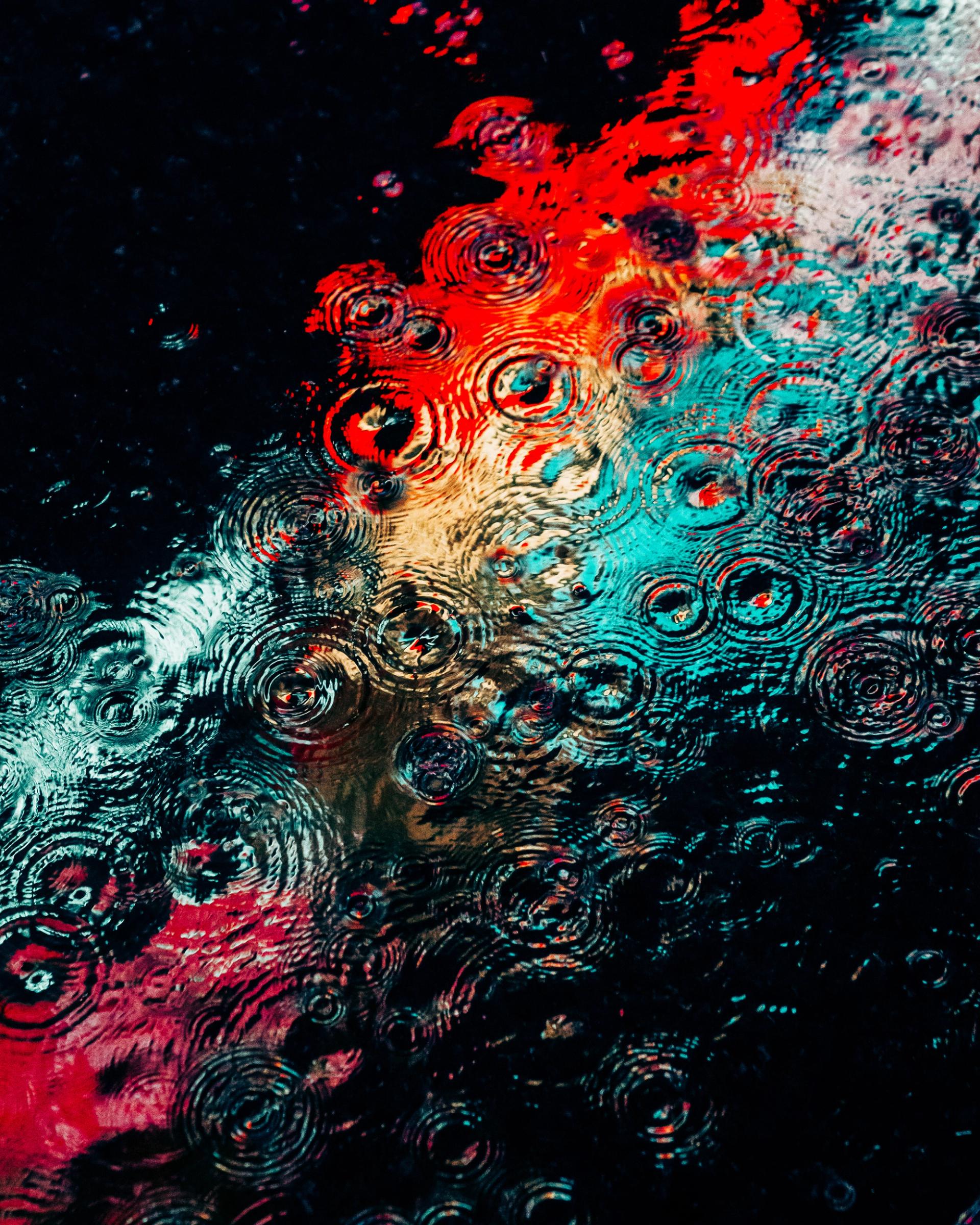 Overlapping raindrop rings in red and teal reflected neon