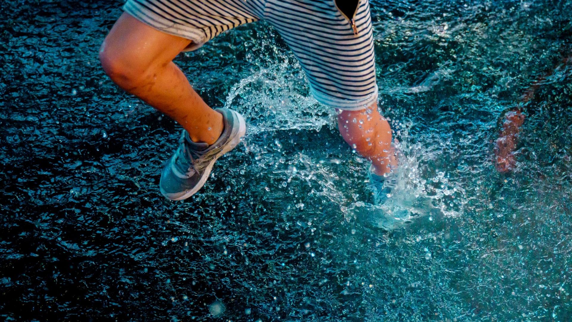 Runner in striped shorts frozen mid-stride, water exploding from a puddle in blue light