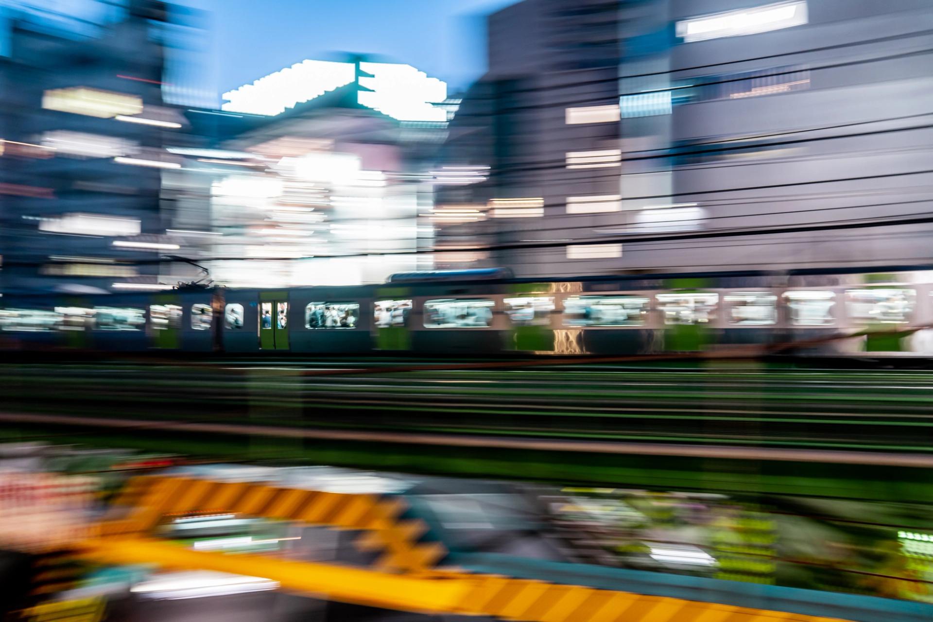 Elevated train panned sharp in daylight, the city behind it streaked into horizontal lines