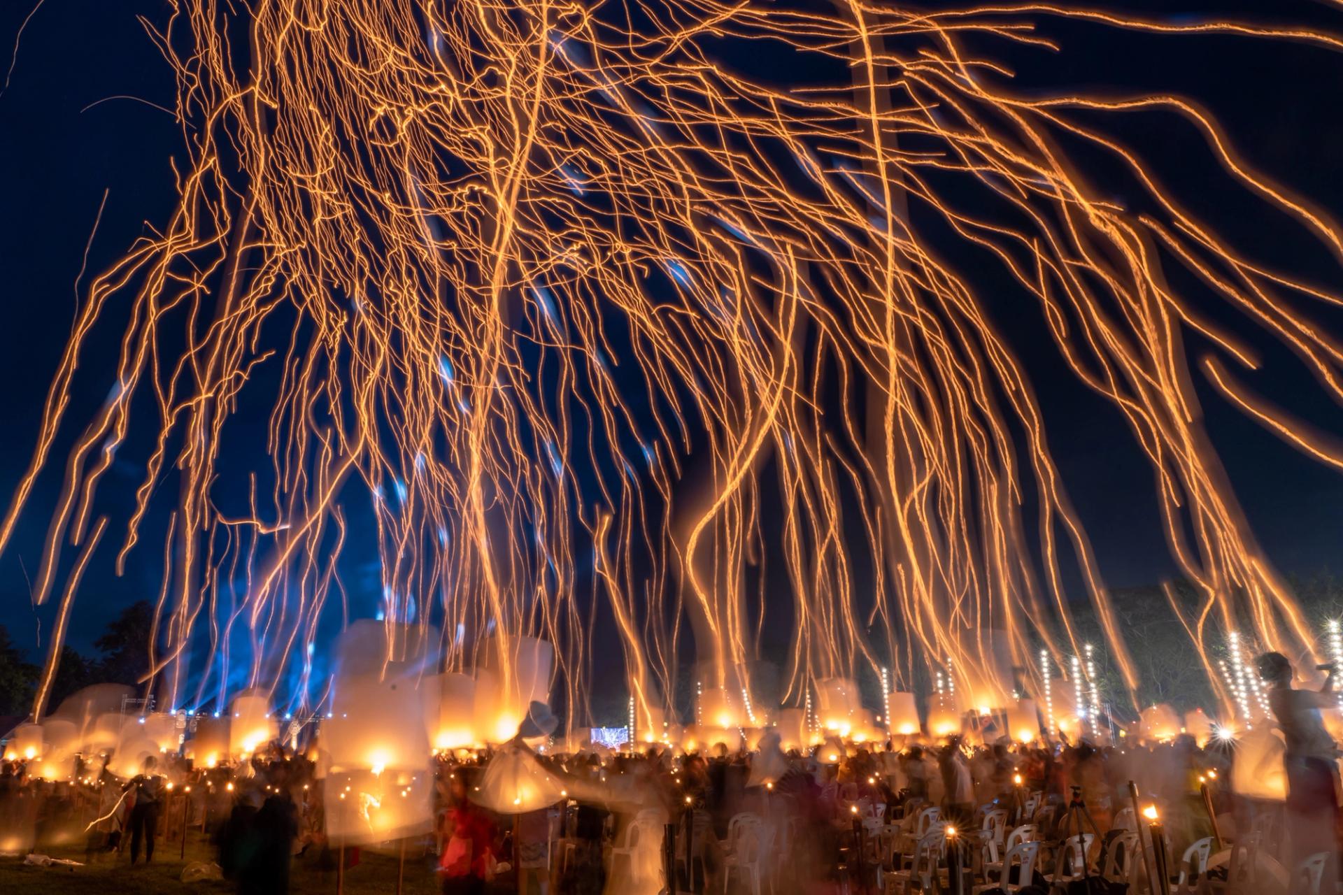 Long exposure of a lantern festival, hundreds of sky lanterns rising as glowing orange trails above a crowd