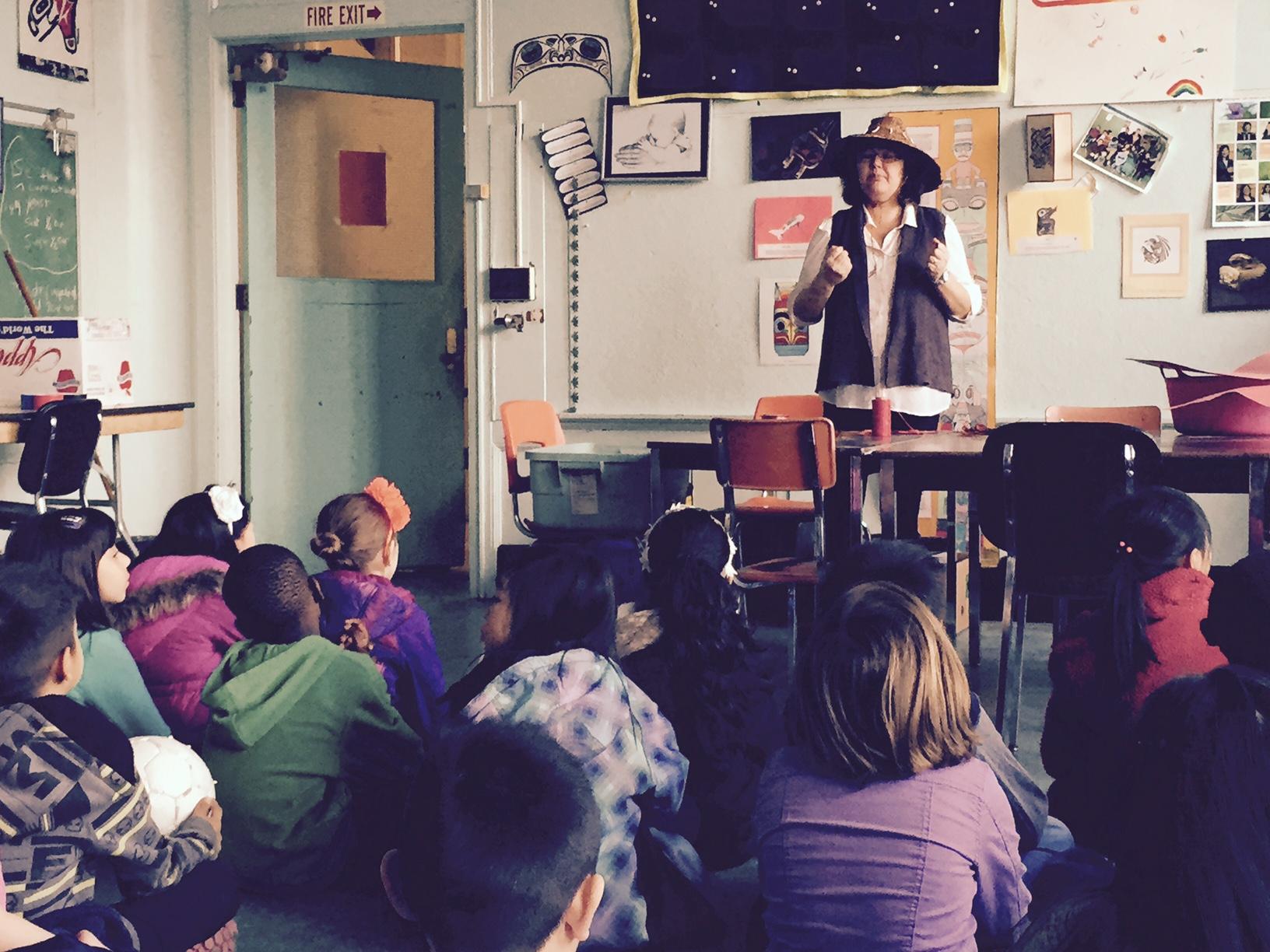 A speaker in a wide-brimmed hat addresses a classroom of seated children at Strathcona Elementary