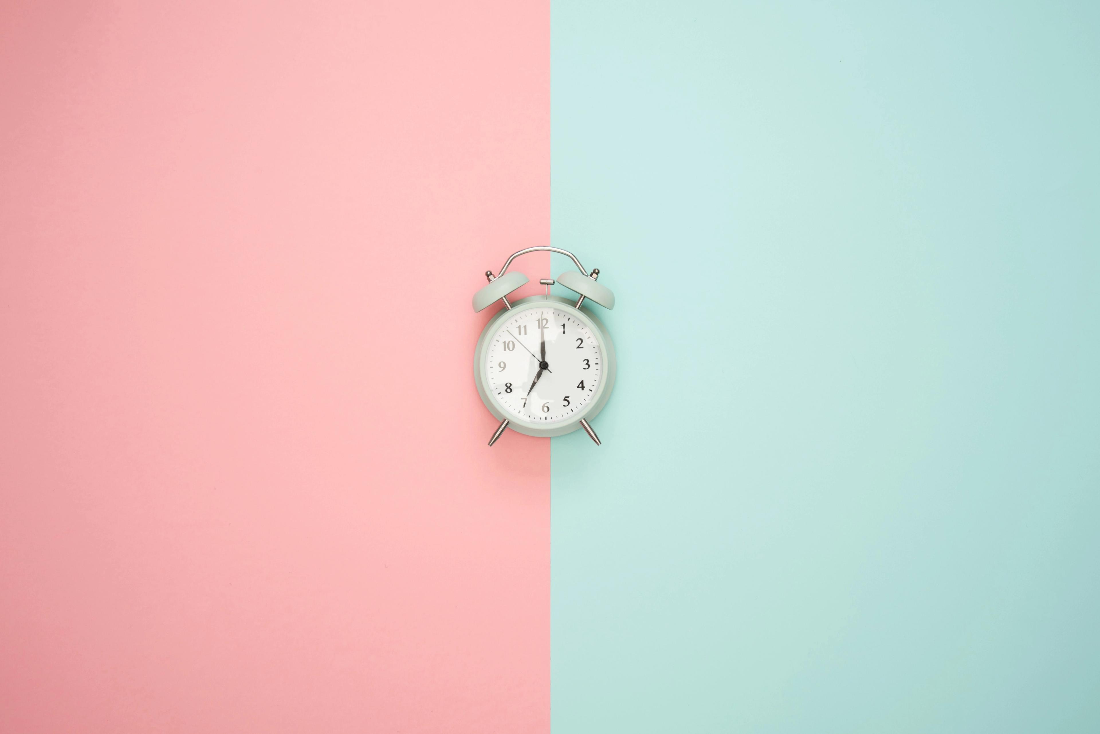 A white alarm clock against a split pink and mint background