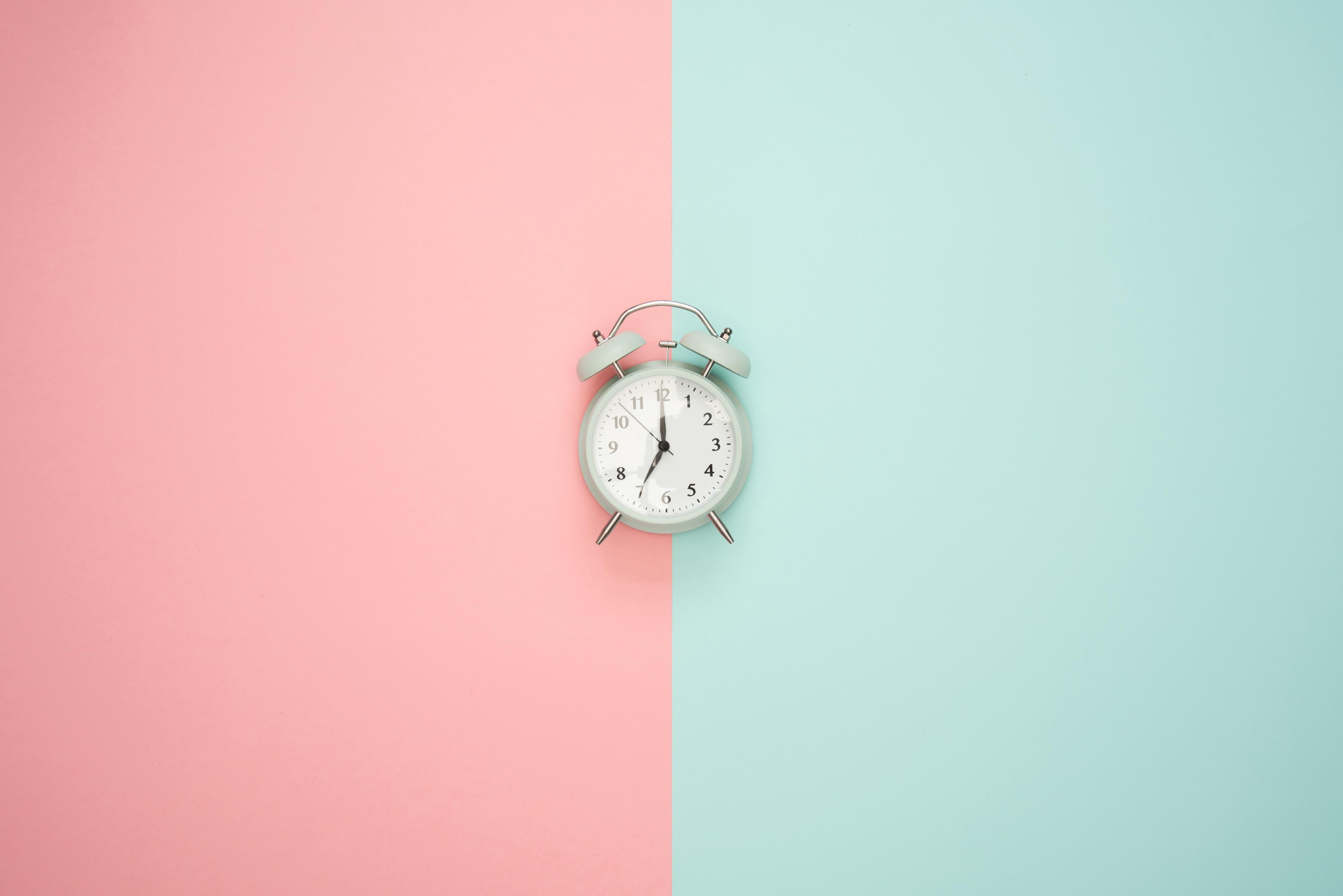 A white alarm clock against a split pink and mint background
