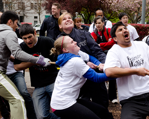 Students in white CLICK T-shirts strain against the rope, leaning back and shouting