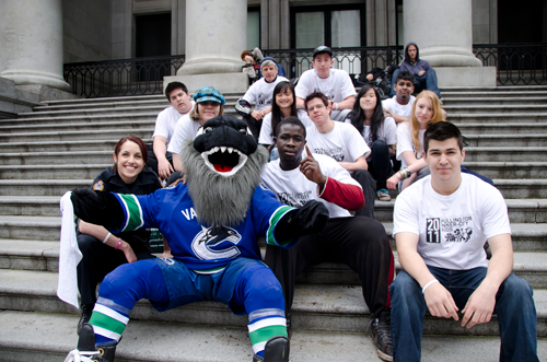 Fin, the Vancouver Canucks mascot, sits on the Art Gallery steps surrounded by students and volunteers