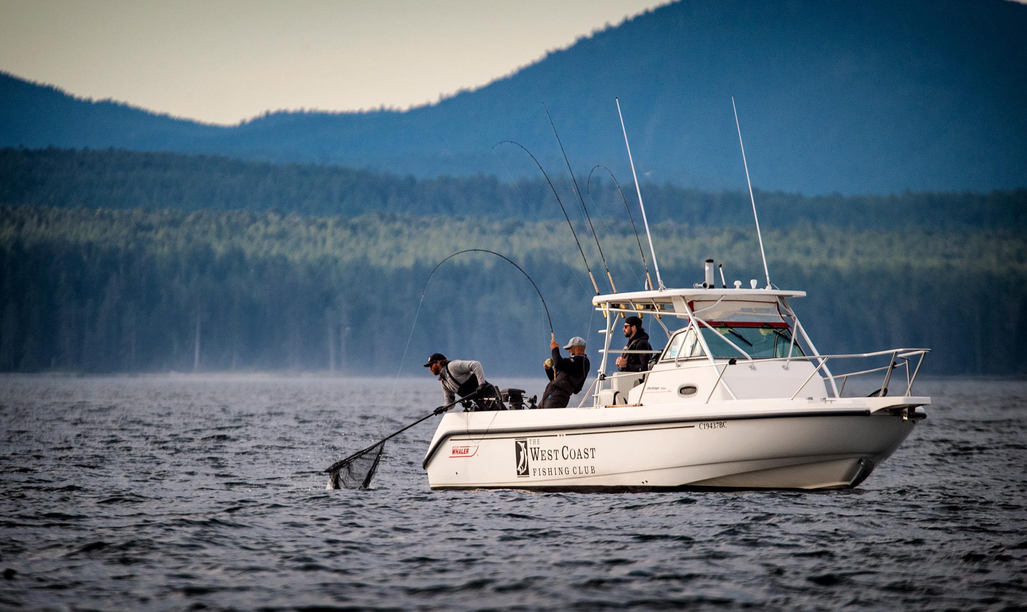 A West Coast Fishing Club boat on calm water below forested mountains in Haida Gwaii