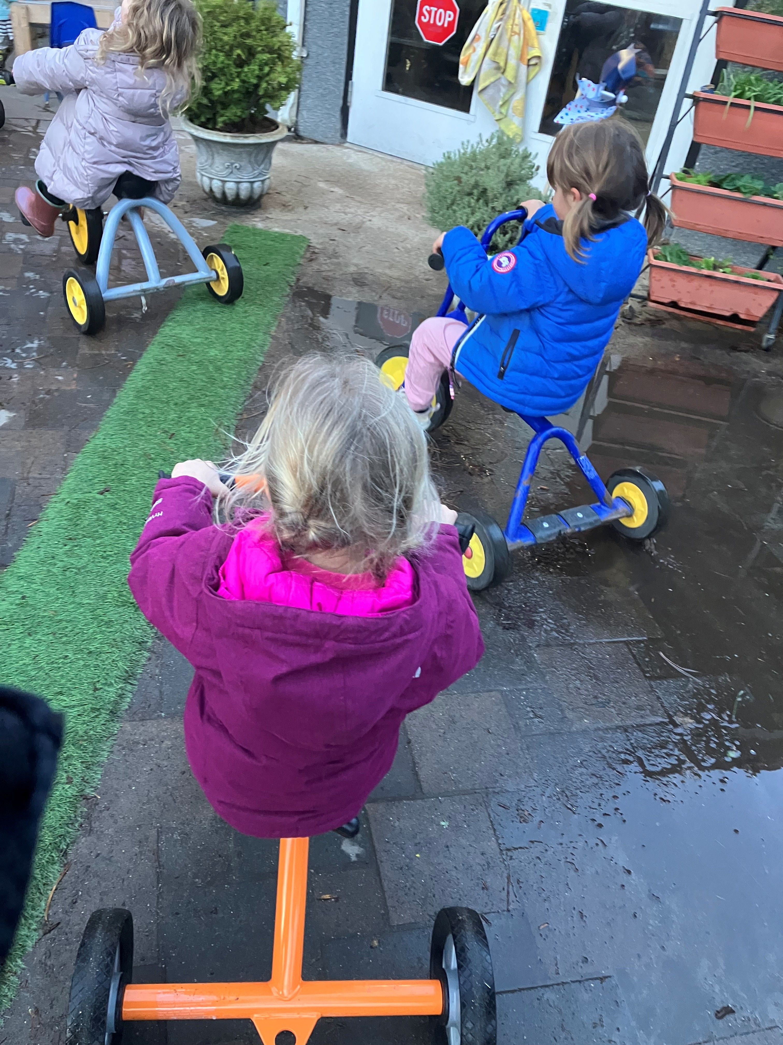 Children riding tricycles outdoors, photographed from behind
