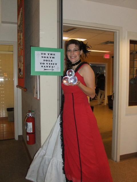 A performer in a red gown beside a sign pointing to the North Pole