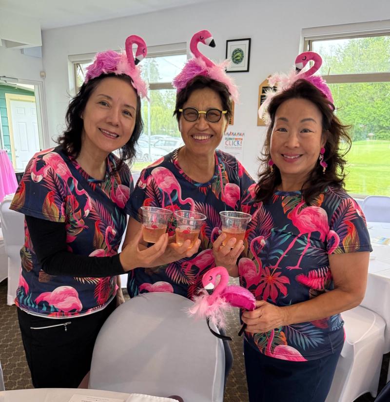 Three players in matching flamingo-print shirts and pink flamingo headbands raise a toast in the clubhouse.