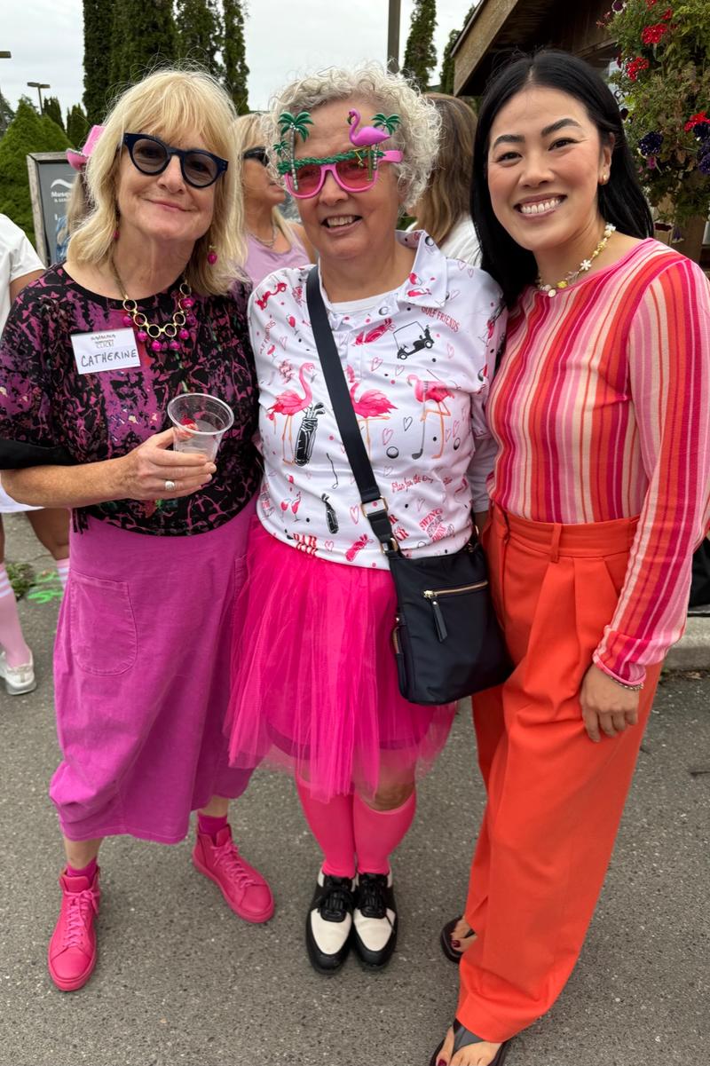 Three guests in pink and orange outfits smile together outside the clubhouse.