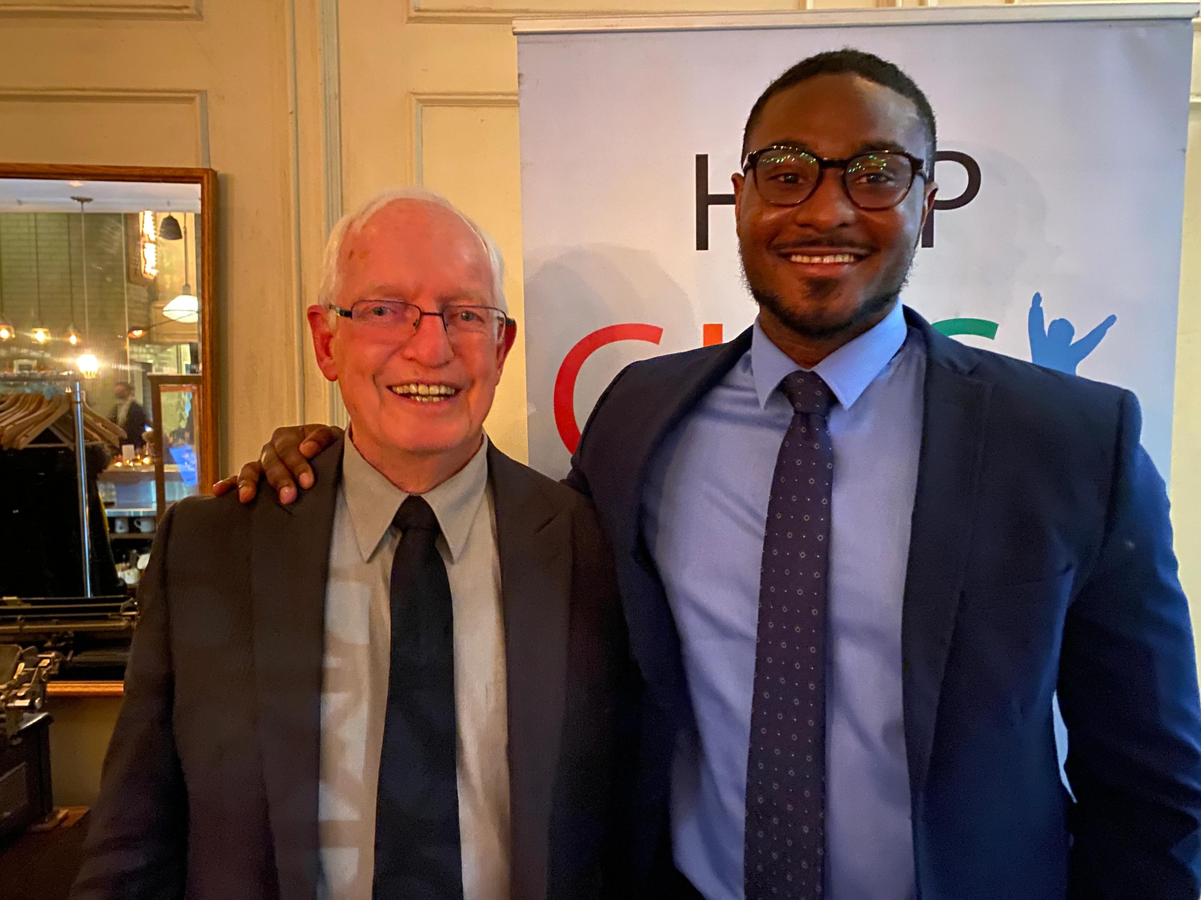 CLICK director Mike Evans with keynote speaker Osaro Obaseki in front of the Help CLICK Help Kids banner