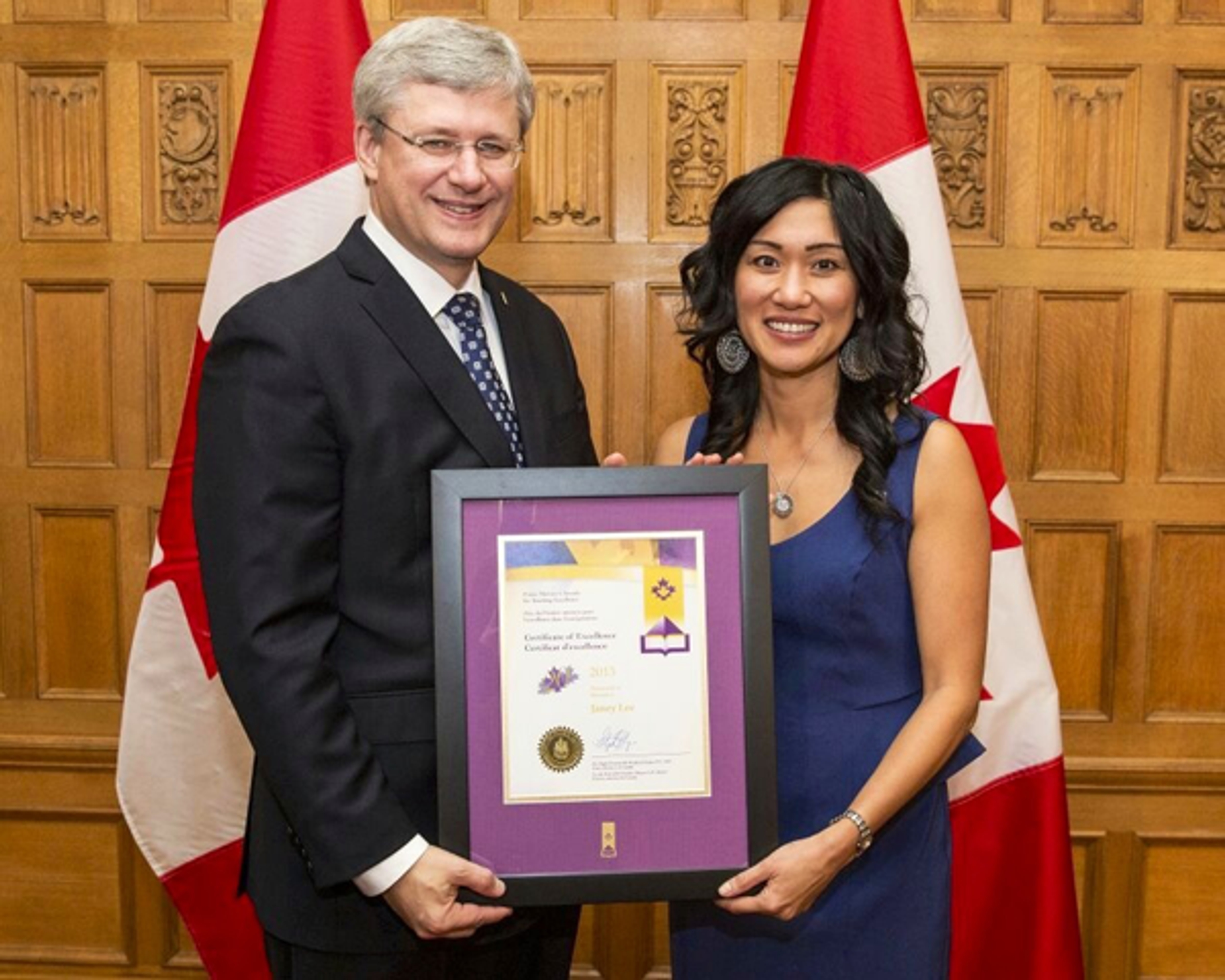 Janey Lee receives her framed Prime Minister's Award for Teaching Excellence, standing between Canadian flags