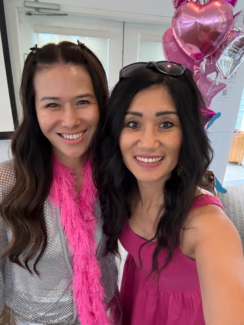 Two smiling players pose for a selfie in the clubhouse in front of pink heart-shaped balloons.