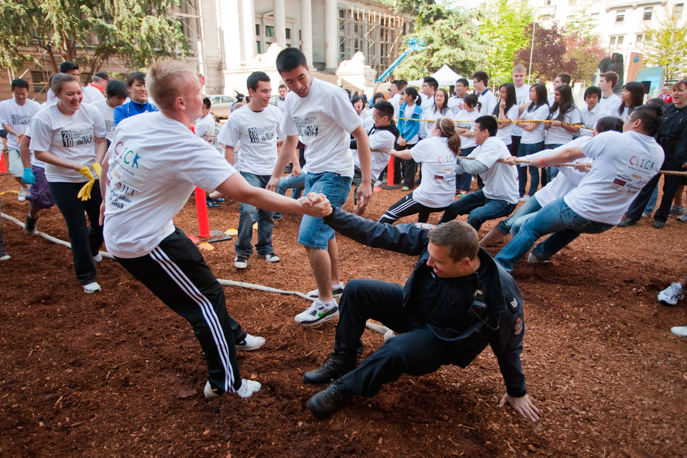 Two teams in white CLICK T-shirts pull hard against each other on the tug of war rope, one puller down on the ground