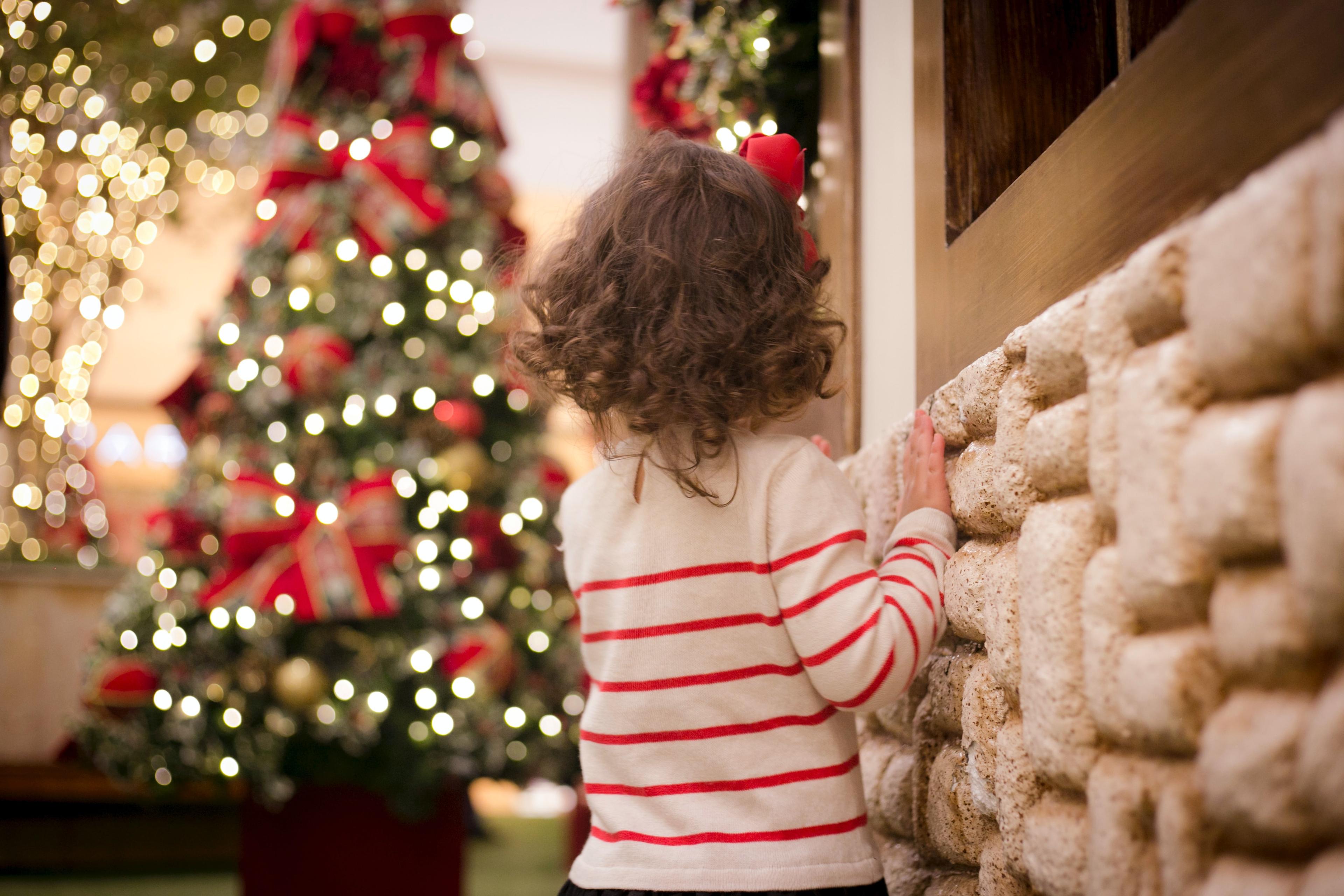 A young child in a striped shirt looking at a lit Christmas tree