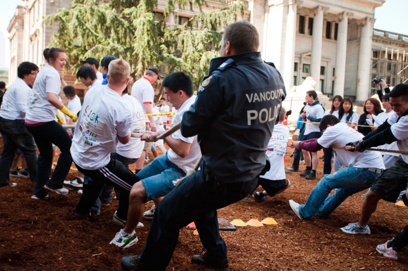 A Vancouver Police officer, back to the camera, pulls at the head of a student team