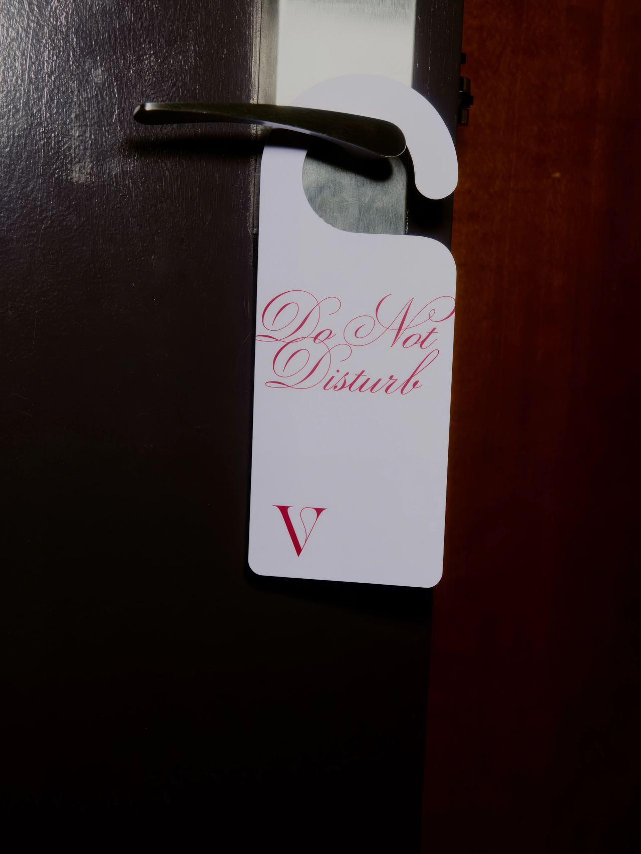 A Do Not Disturb hanger with a pink V monogram on a door handle