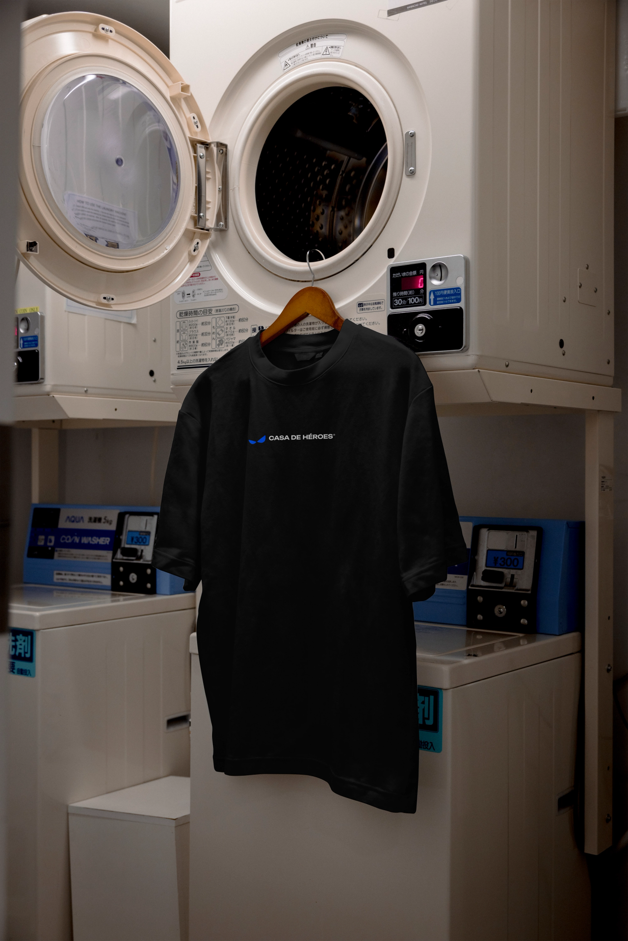 A black Casa de Héroes T-shirt hanging from an open dryer in a coin laundry