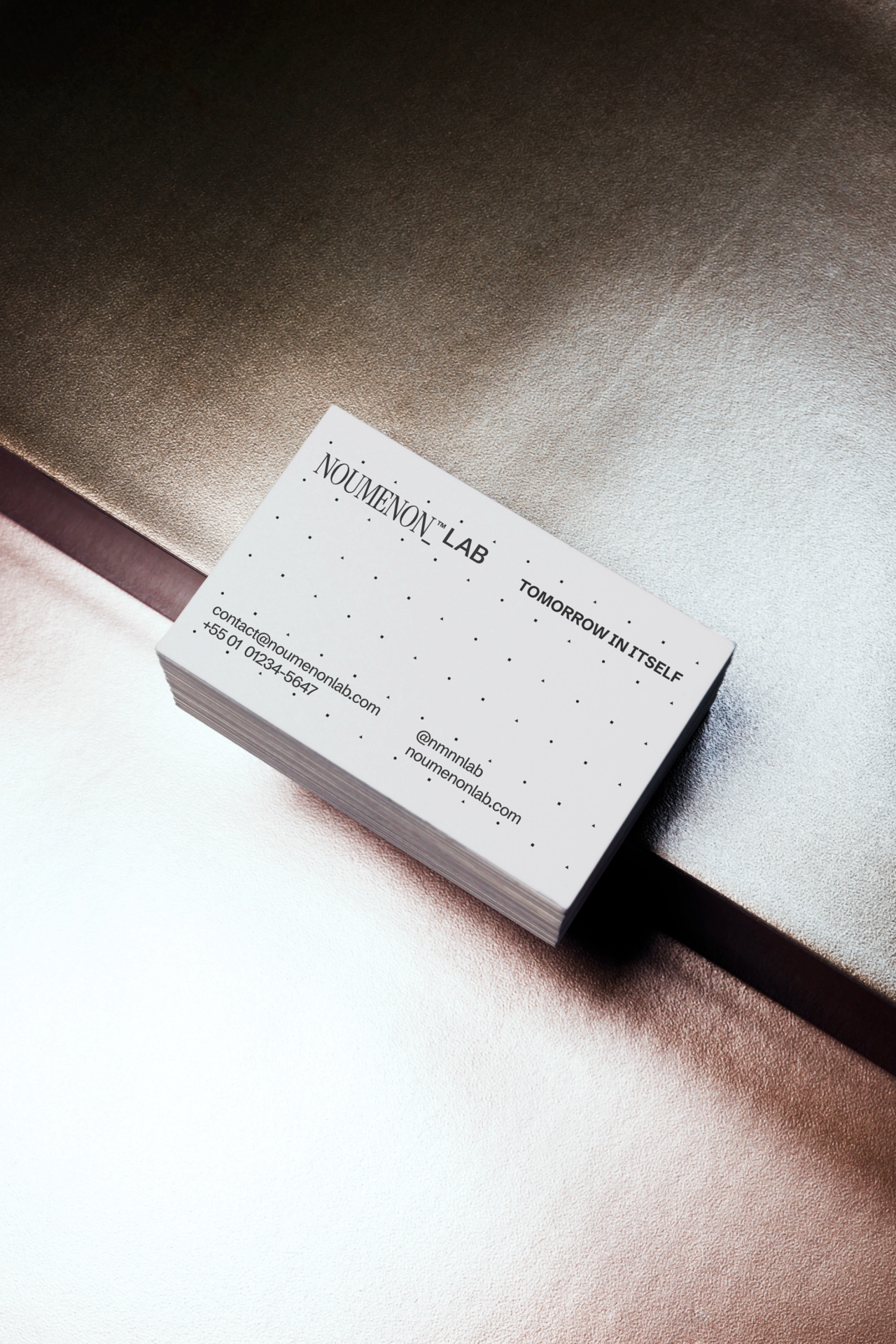 A stack of NOUMENON LAB business cards with a dot grid on a metallic surface