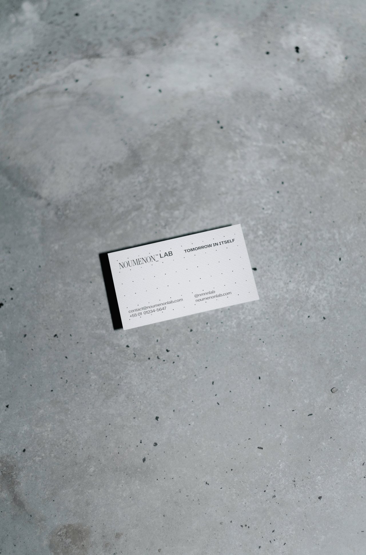A single NOUMENON LAB business card reading "Tomorrow in itself" on grey concrete