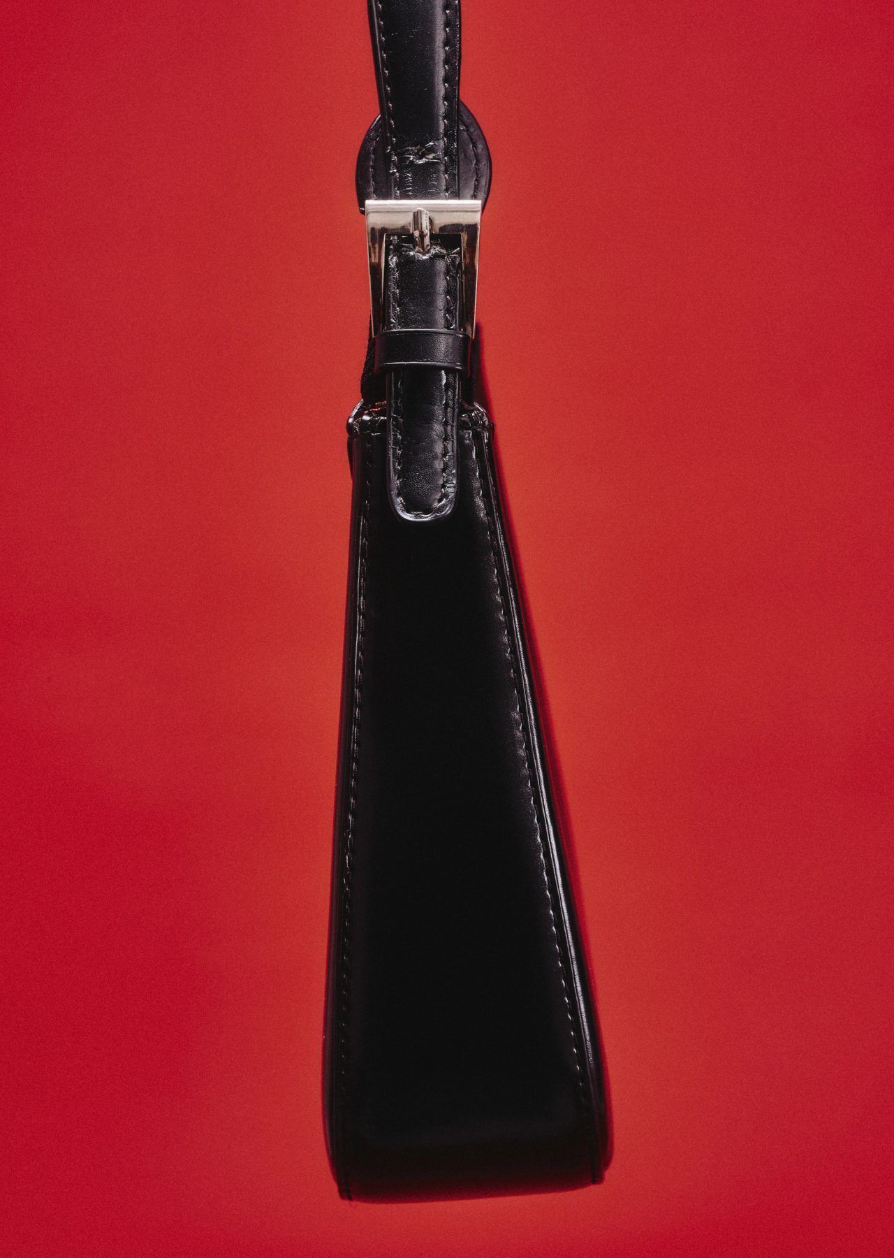 A black leather shoulder bag with a silver buckle against red