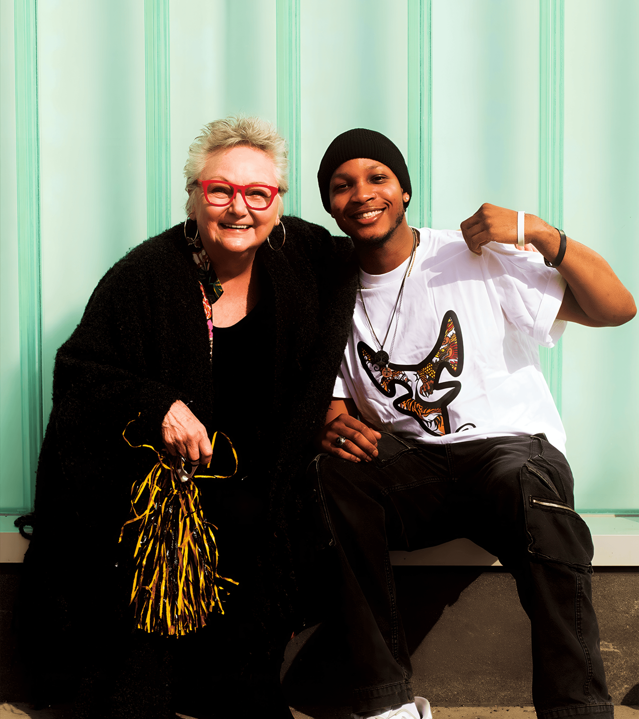 A man in a D2R tee and a woman in red glasses by a mint wall