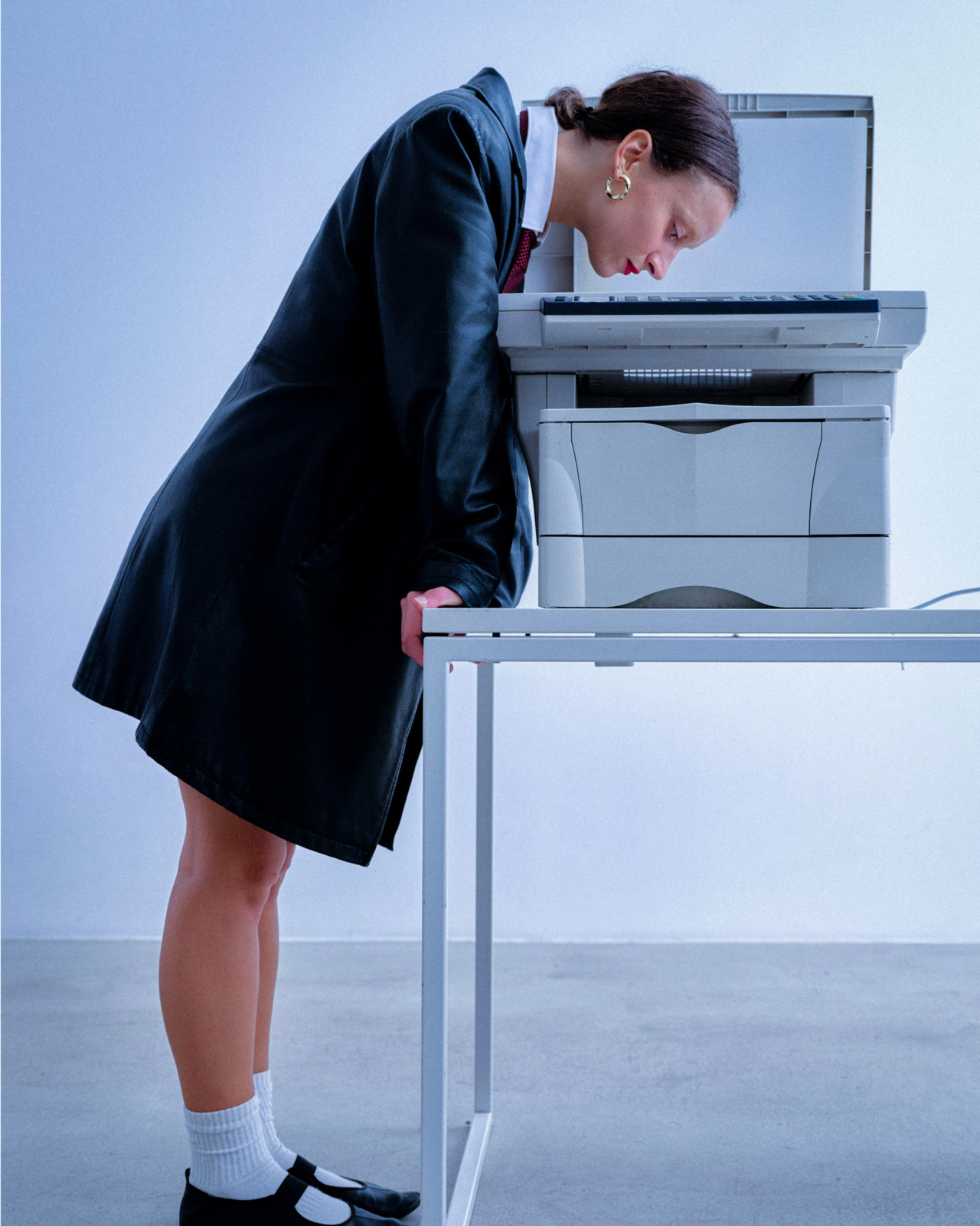 A model in a leather coat bending over a photocopier on a white desk