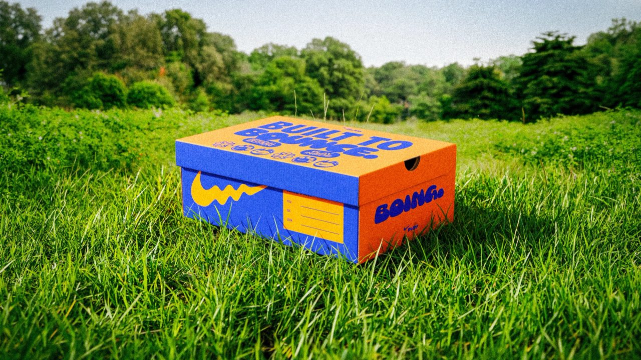 Orange and blue shoebox on grass, its lid reading Built to Bounce, with a wavy swoosh